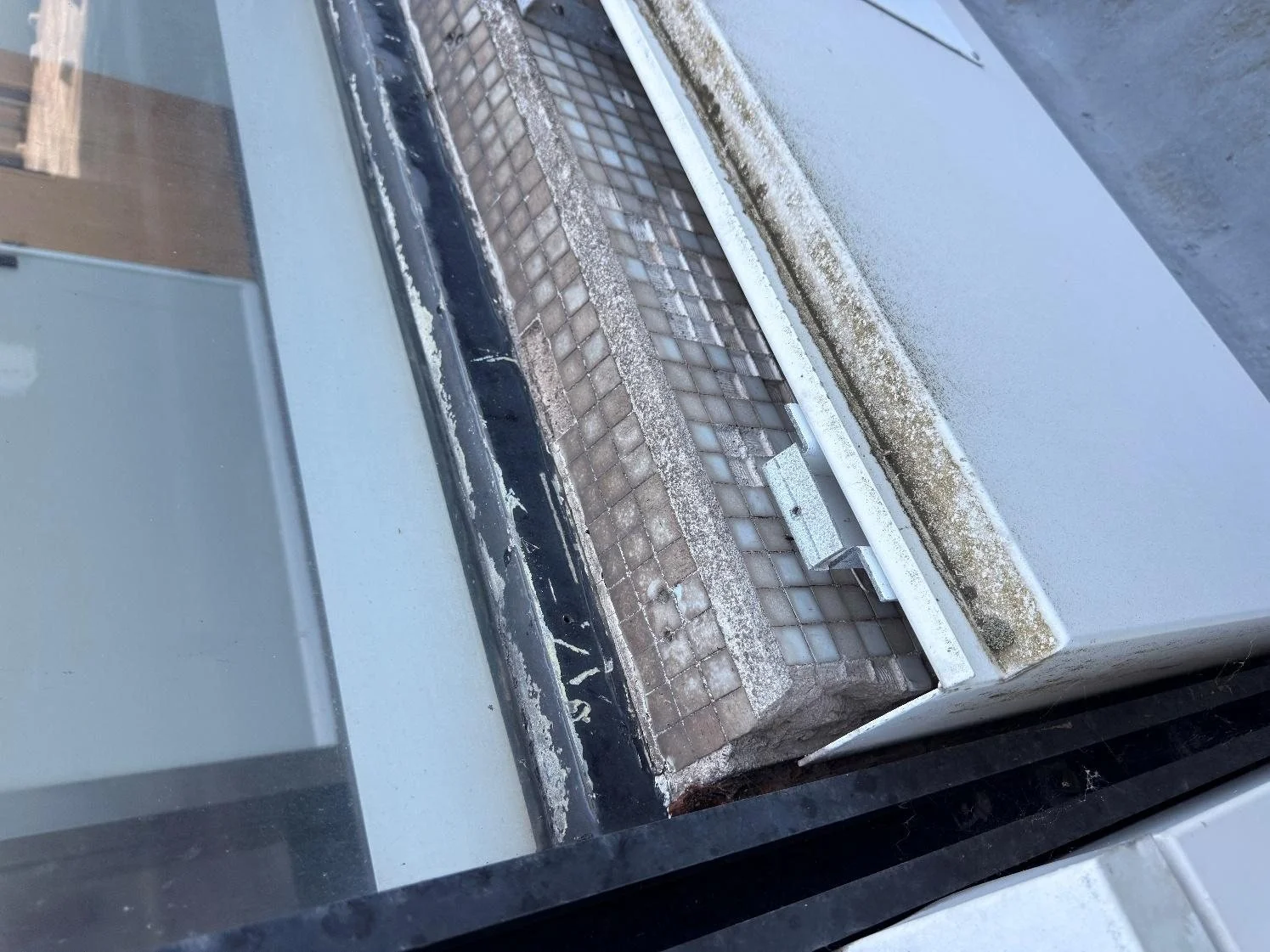 Window sill cladding cut back to expose the original ceramic mosaic tiles on the concrete wall