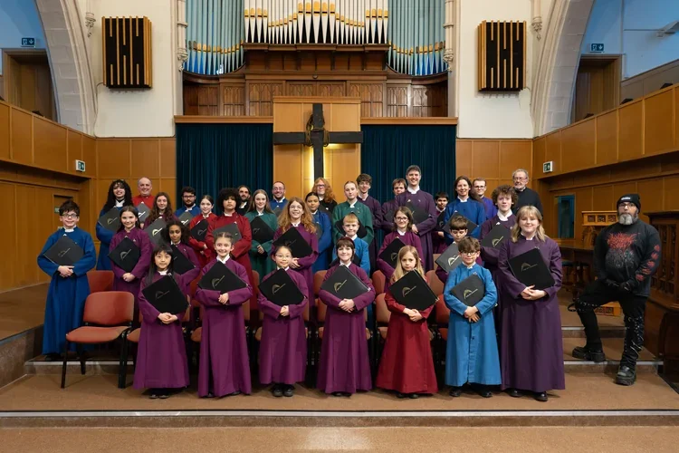 Choir members posing in coloured robes in front of the organ at Highfield Trinity Church