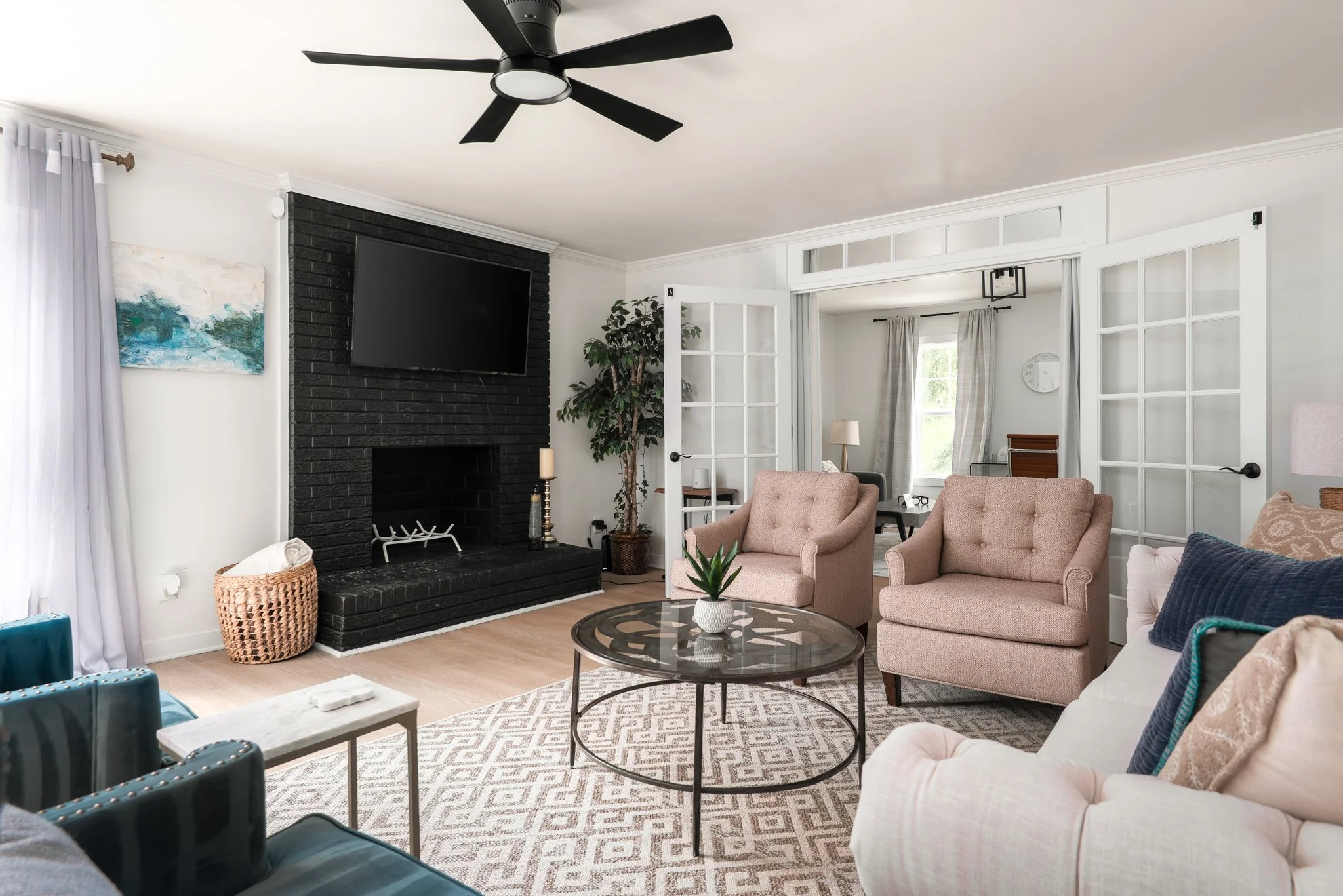 Contemporary room with cream couch, beige chairs, white weave pattern rug, fireplace with mounted TV, and double french doors