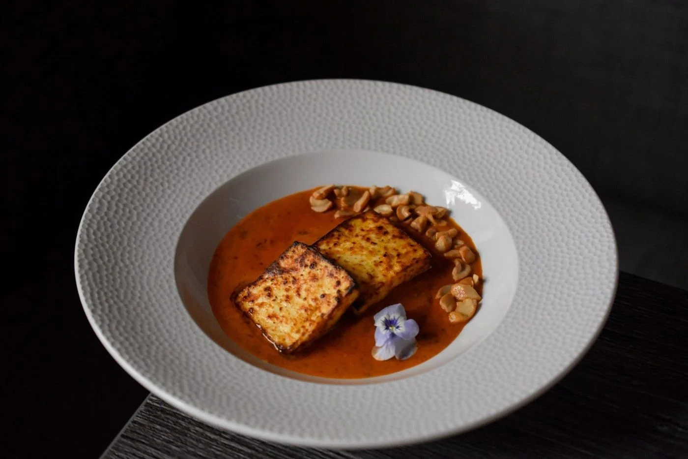Paneer Butter Masala with two seared paneer pieces and cashews around the side
