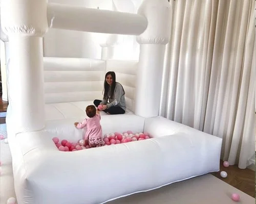 White toddler bounce house set up indoors with soft lighting and curtains