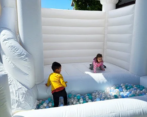 Kids playing in Twisty Castle bounce house with blue and white ball pit and fun twisty slide