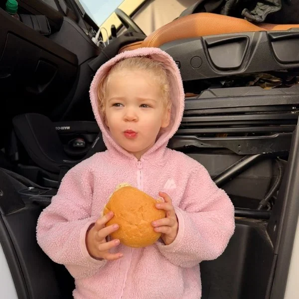 Little one with a bread roll by the van