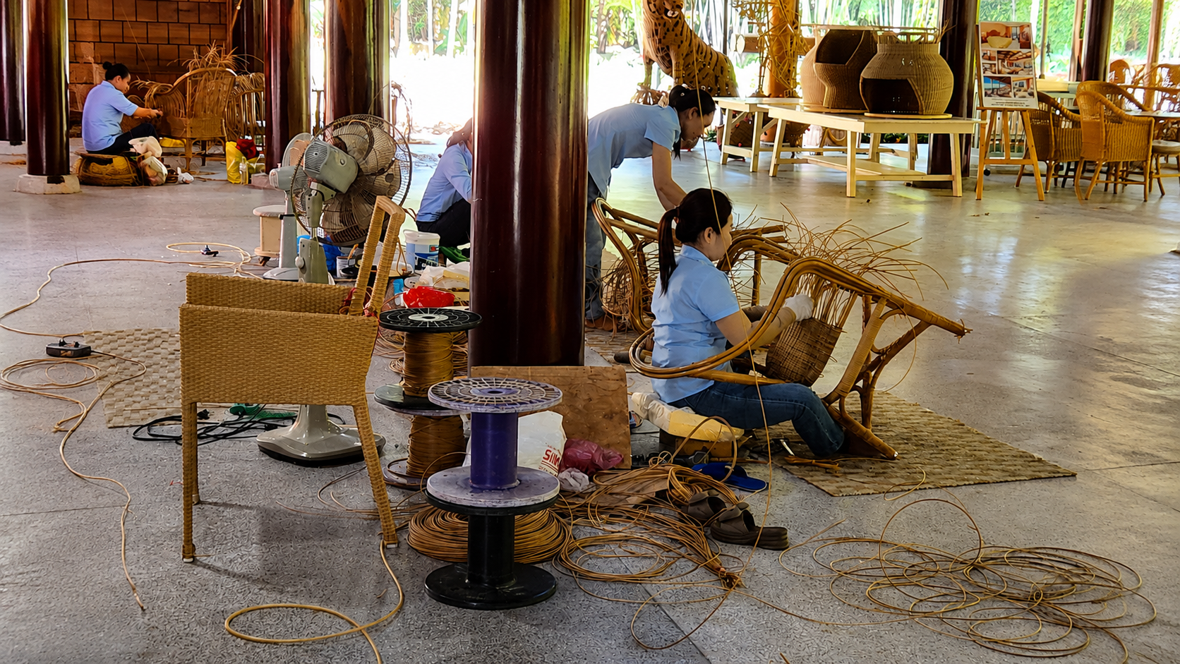 Professional buyer walking through a well-organized Vietnamese rattan furniture production facility with artisans working at weaving stations