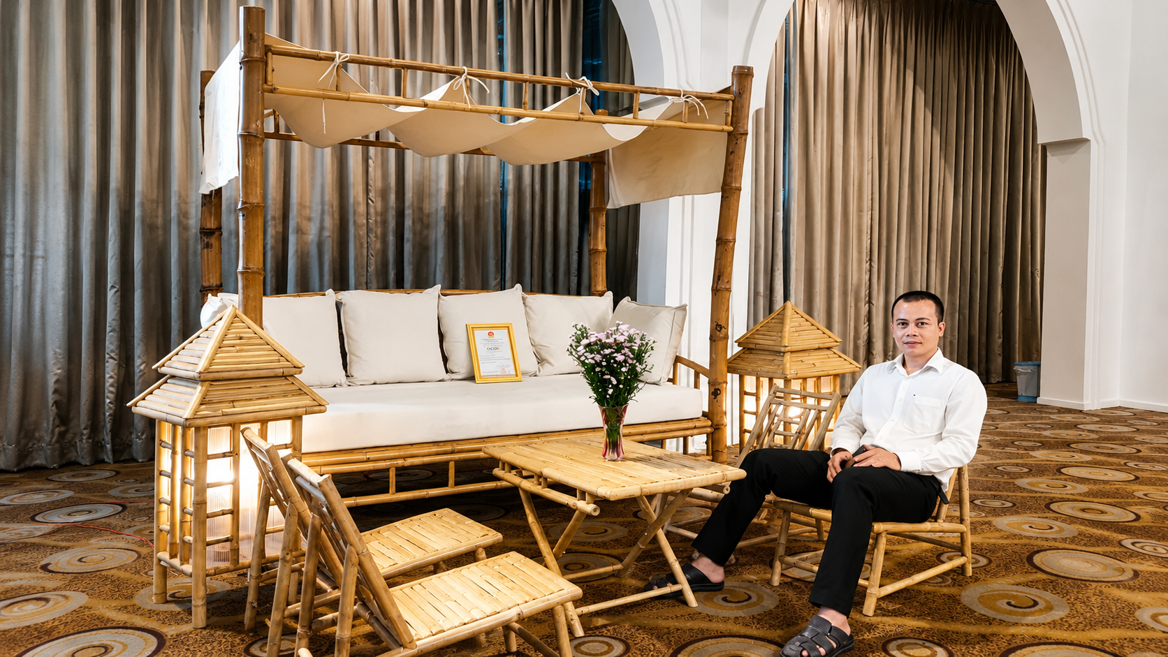 A coordinated bamboo furniture and accessories collection displayed at a Vietnamese trade exhibition, including a canopy daybed, folding chairs, and pagoda lanterns