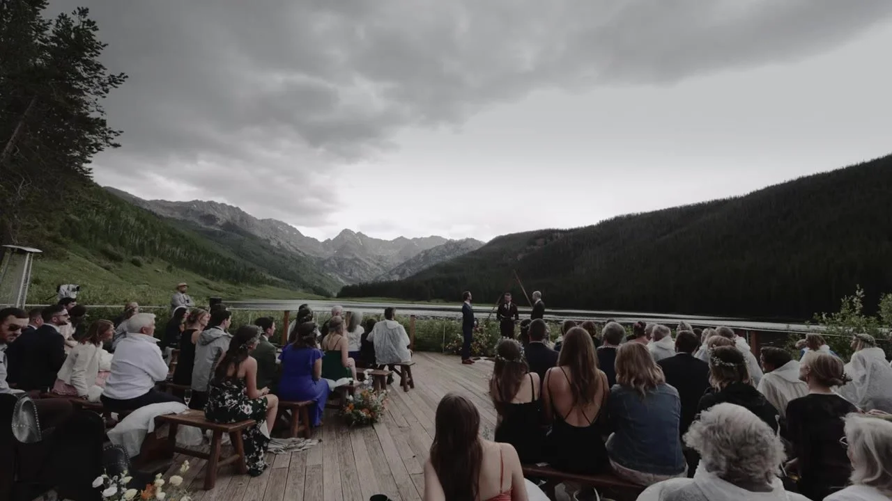 Wide ceremony on the Piney River Ranch deck under a heavy sky with Piney Lake and the Gore Range