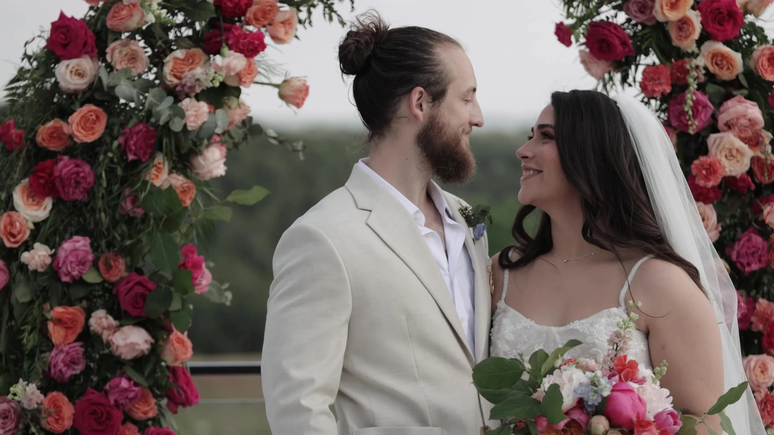 Peter and Kiyara smiling close among pink florals during their ceremony at Videre Estate Austin