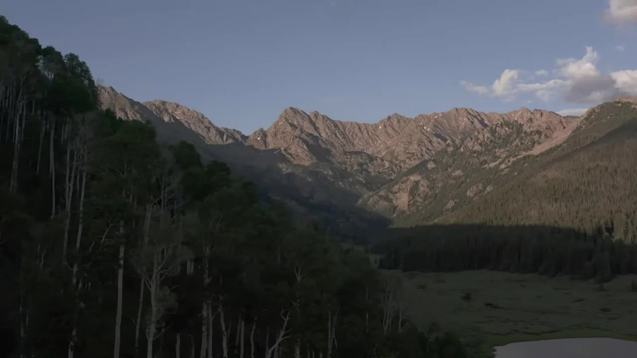 Gore Range peaks in warm light above forest and a sliver of lake at Piney River Ranch