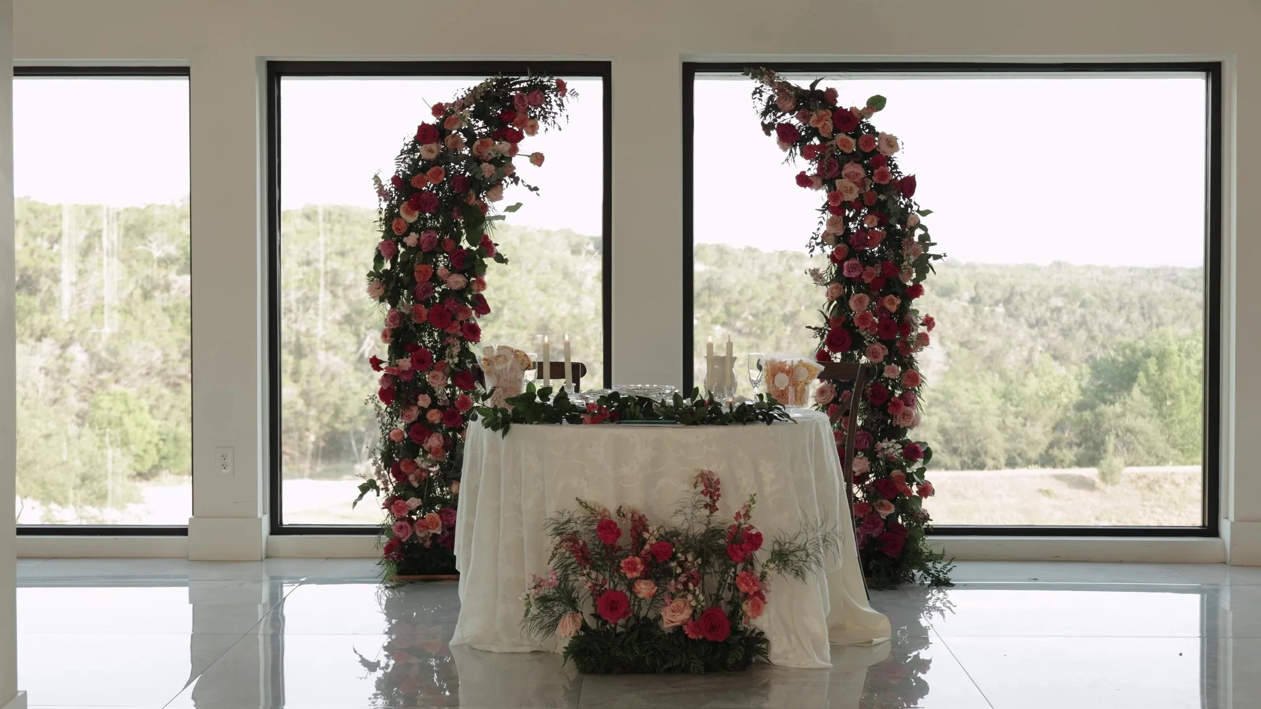 Sweetheart table between tall floral pillars at windows overlooking Texas Hill Country at Videre Estate Austin
