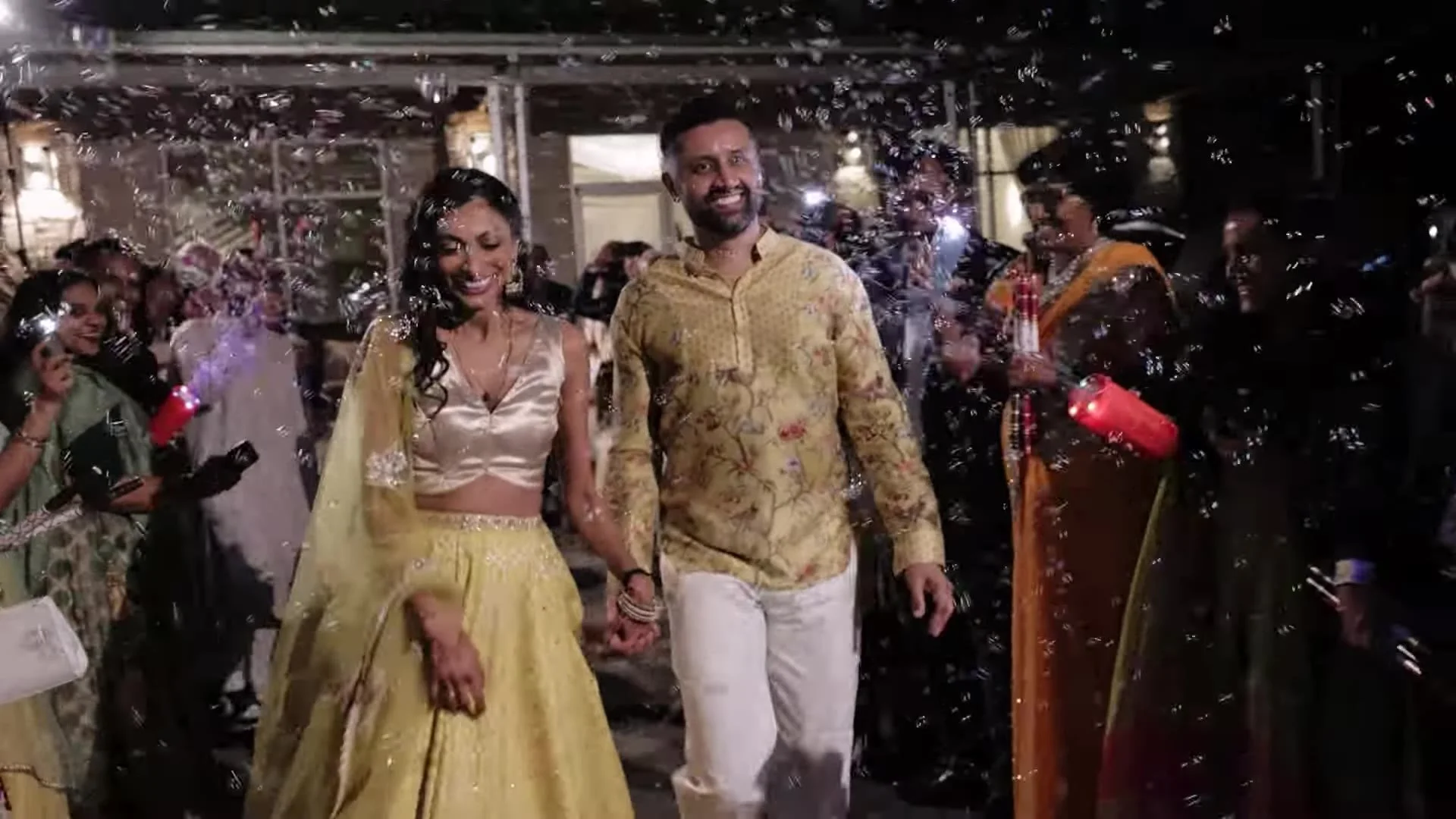 Bhavim and Mala in yellow and gold Indian attire walking through bubbles at their Terrace Club send off in Austin, Texas