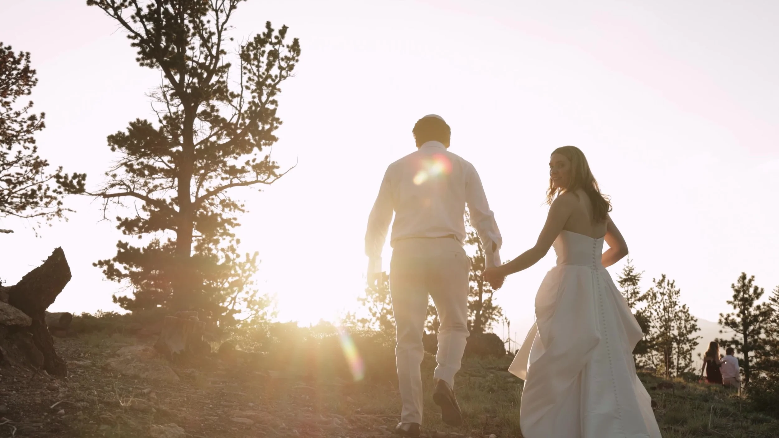 Bride and groom walking into sunset light between pines at Northstar Gatherings in Idaho Springs, Colorado