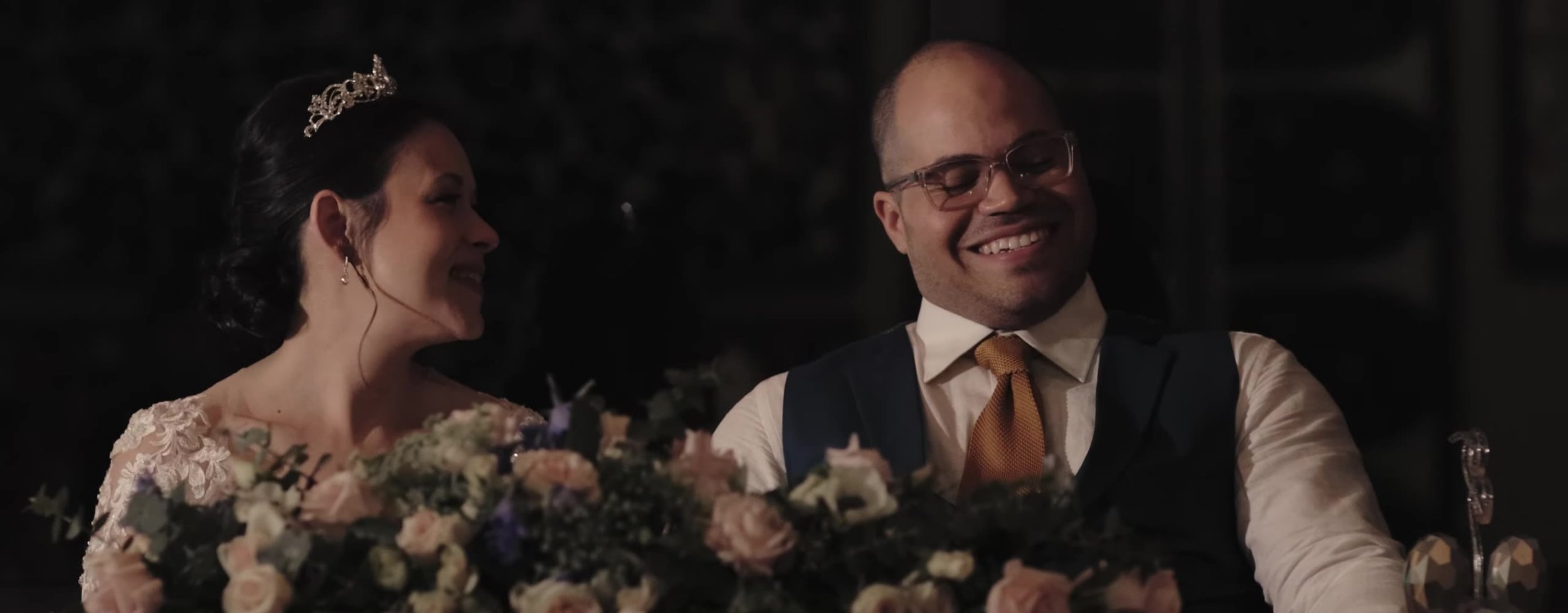 Couple laughing at their sweetheart table, pink and cream roses in front of them