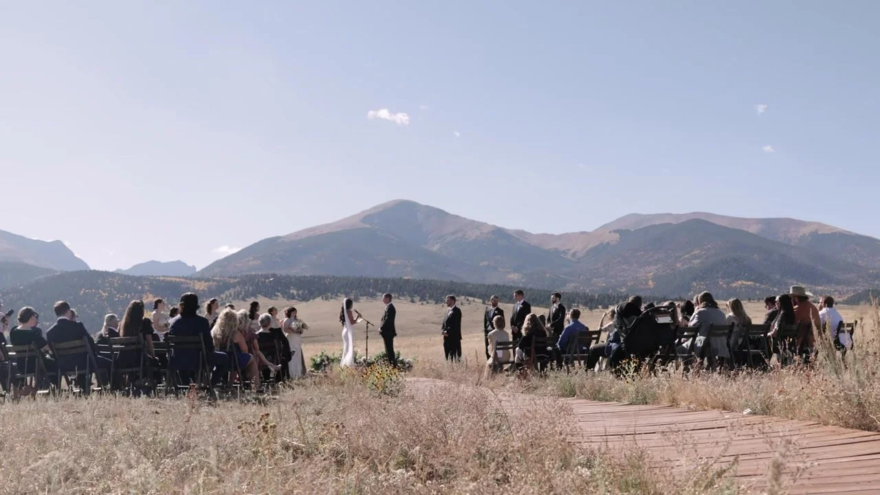 Justin and Sierra at the far end of a wooden plank aisle in a golden meadow under the Wet Mountains at 3 Peaks Ranch