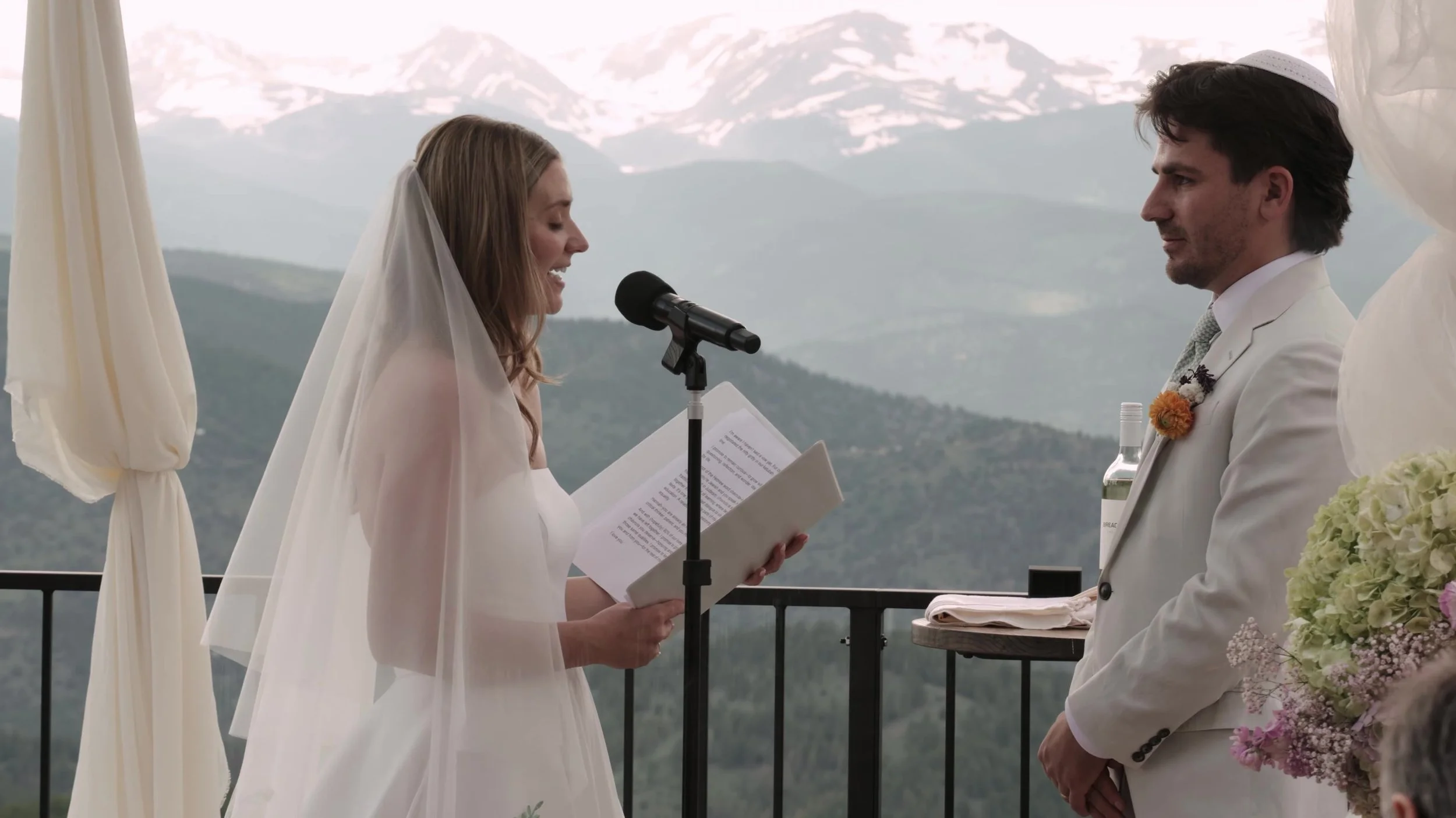 Bride reading vows to the groom on the deck at Northstar Gatherings, snow-capped Colorado mountains behind Idaho Springs