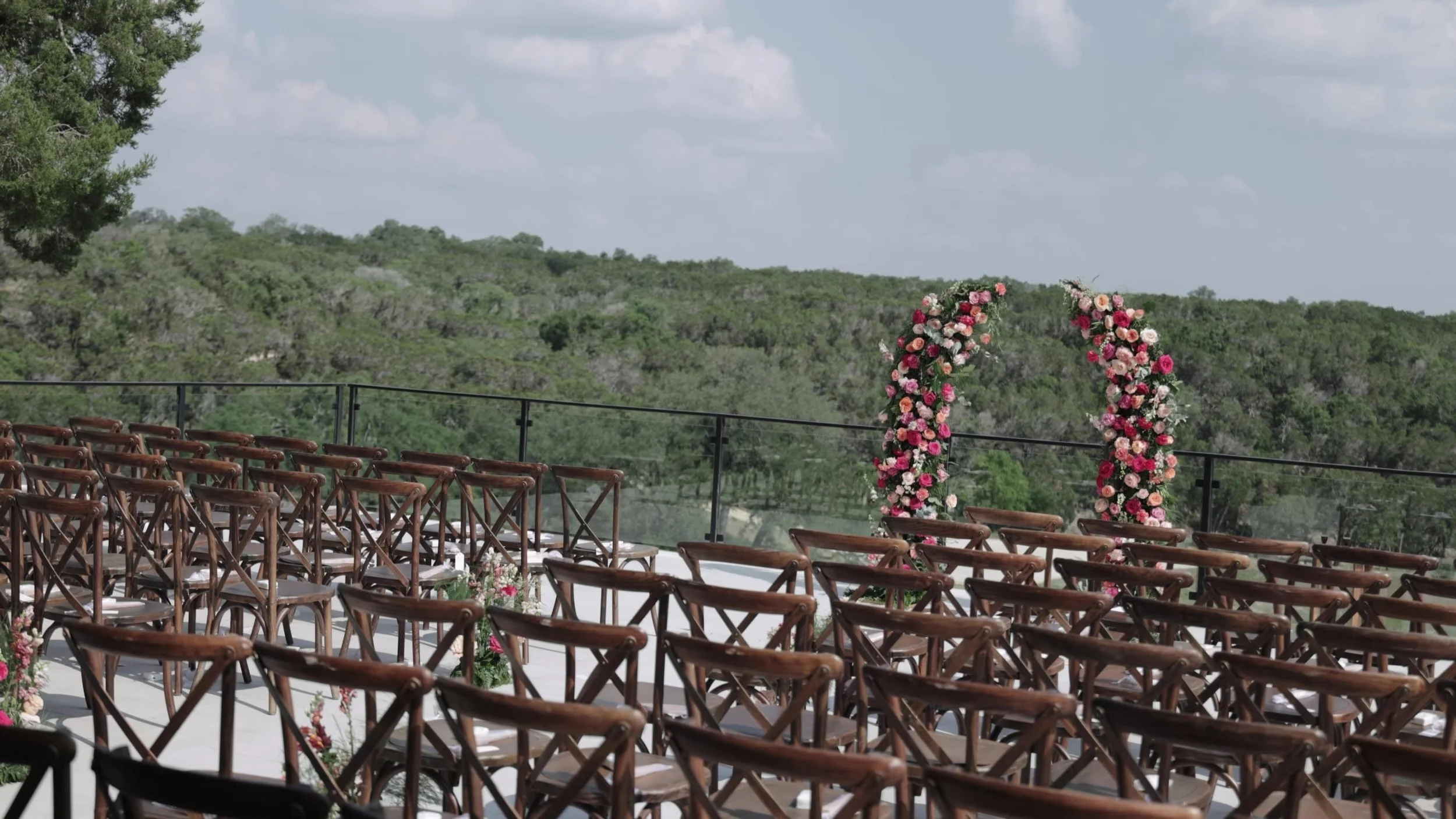 Empty outdoor ceremony chairs facing a floral arch and Texas Hill Country view at Videre Estate near Austin
