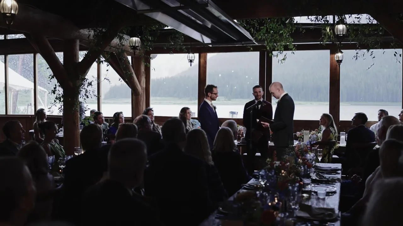 Patrick and Jake exchanging vows inside the Piney River Ranch lodge with the lake in the windows