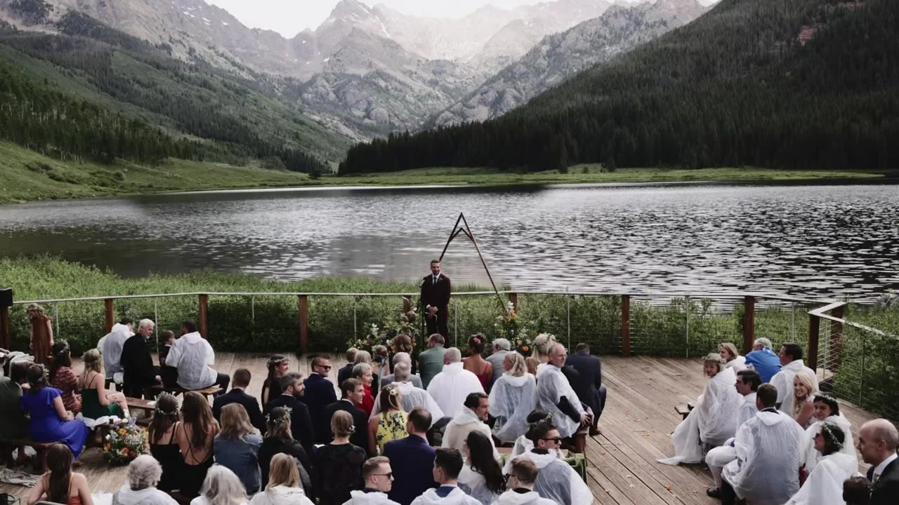 Guests in white rain ponchos on the Piney River Ranch deck facing a triangular lake arch