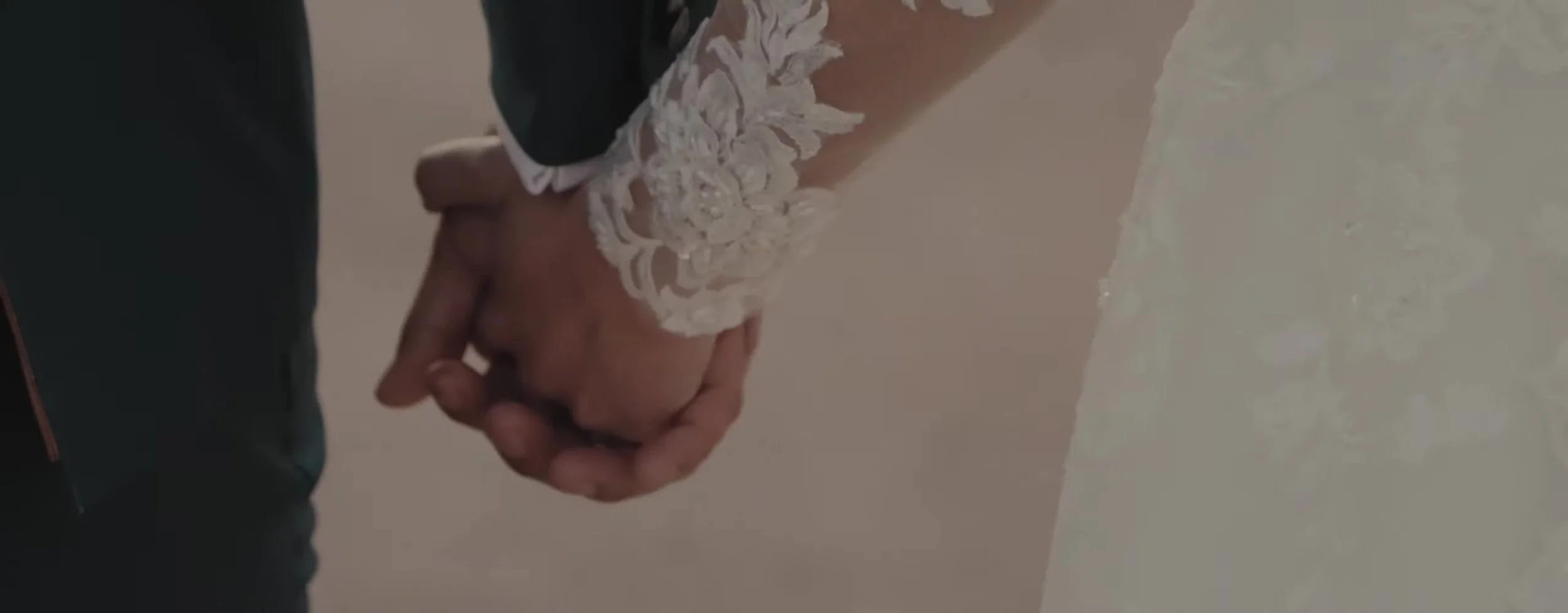 Tight shot of clasped hands, floral lace sleeve against a dark suit cuff