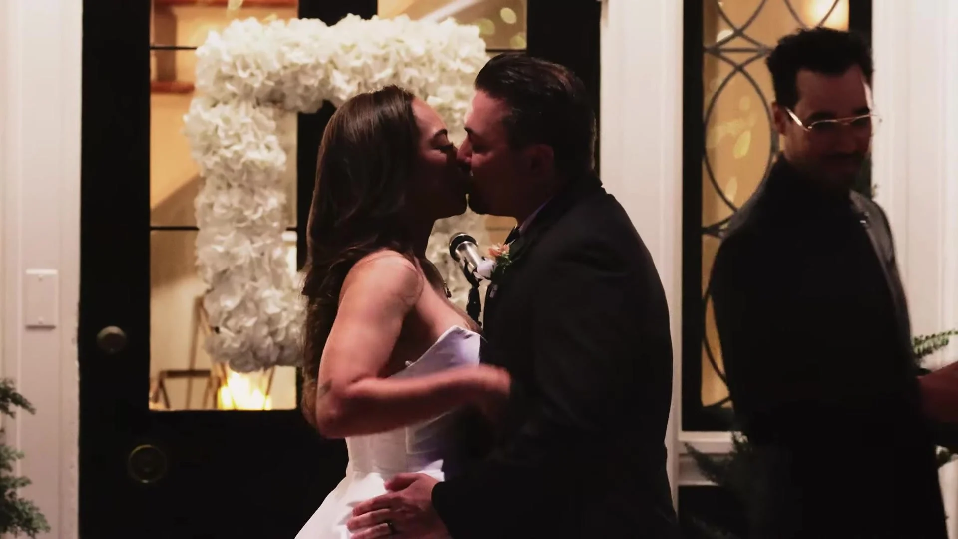 Blair and Gustavo kissing at the Southern Oaks Plantation doorway with a white floral wreath behind them