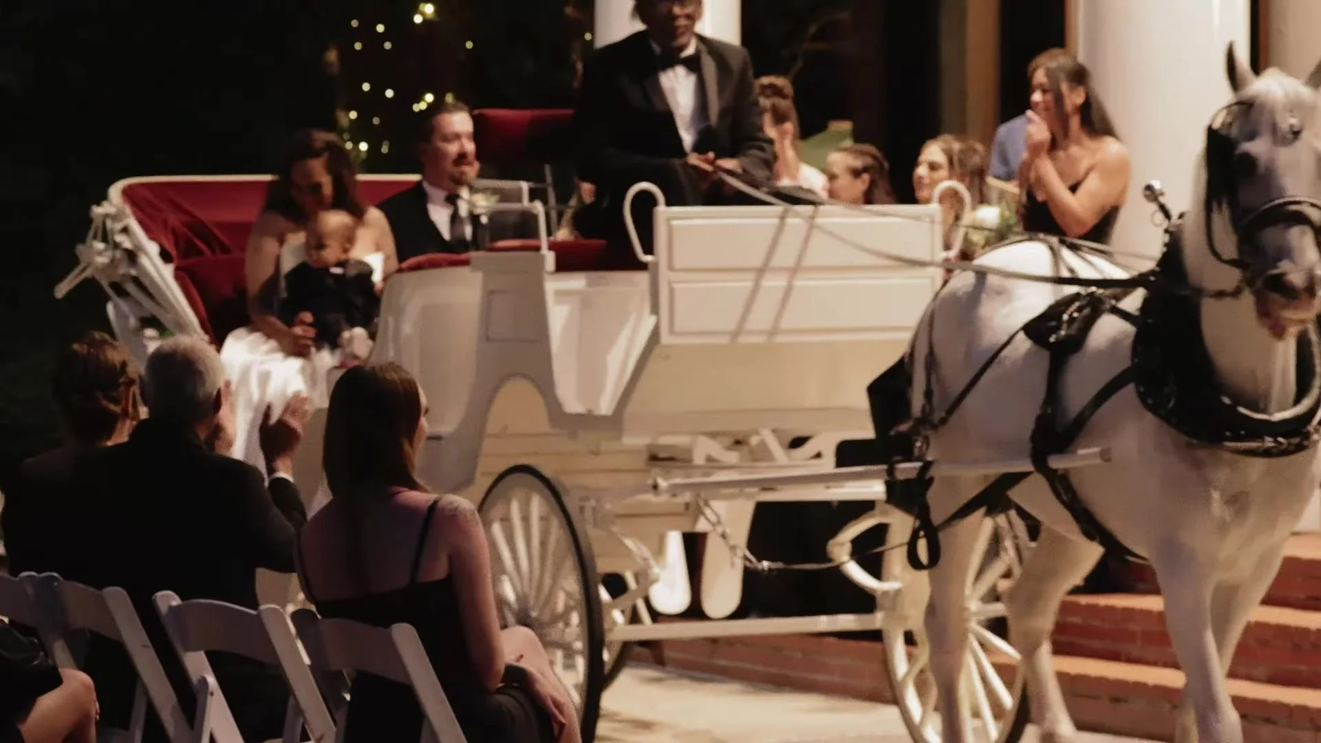 White horse drawn carriage with Blair, Gustavo, and their son in front of Southern Oaks Plantation columns at night