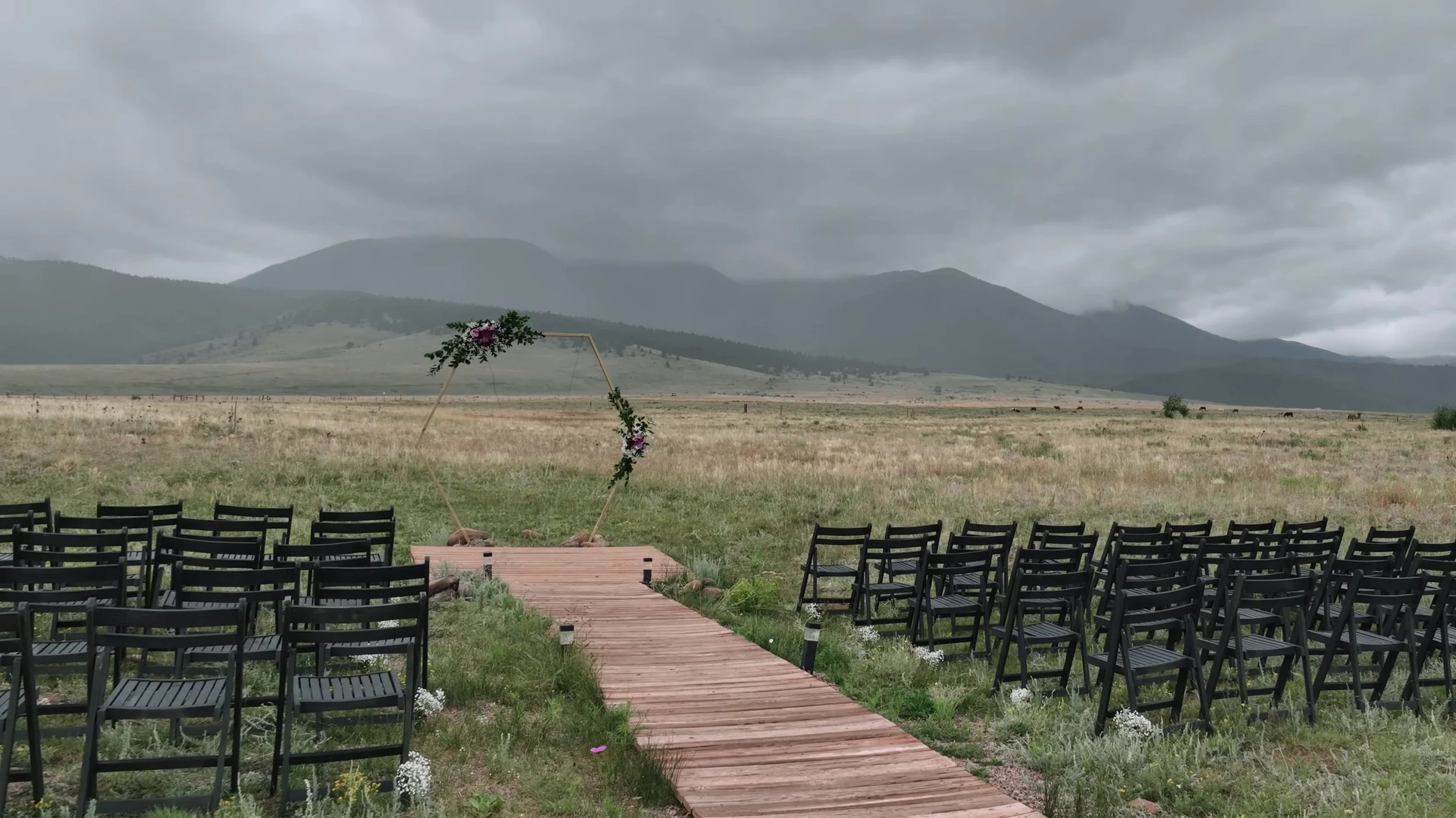 Empty ceremony aisle and hexagonal arch at 3 Peaks Ranch in Westcliffe, Colorado with mountains in cloud