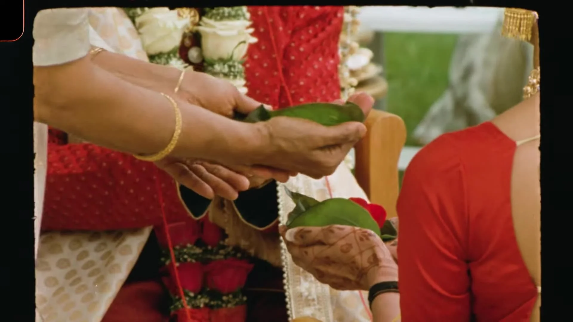 Close up of ritual hands holding green betel leaves and rose petals with mehndi and red attire at Bhavim and Mala's Austin wedding