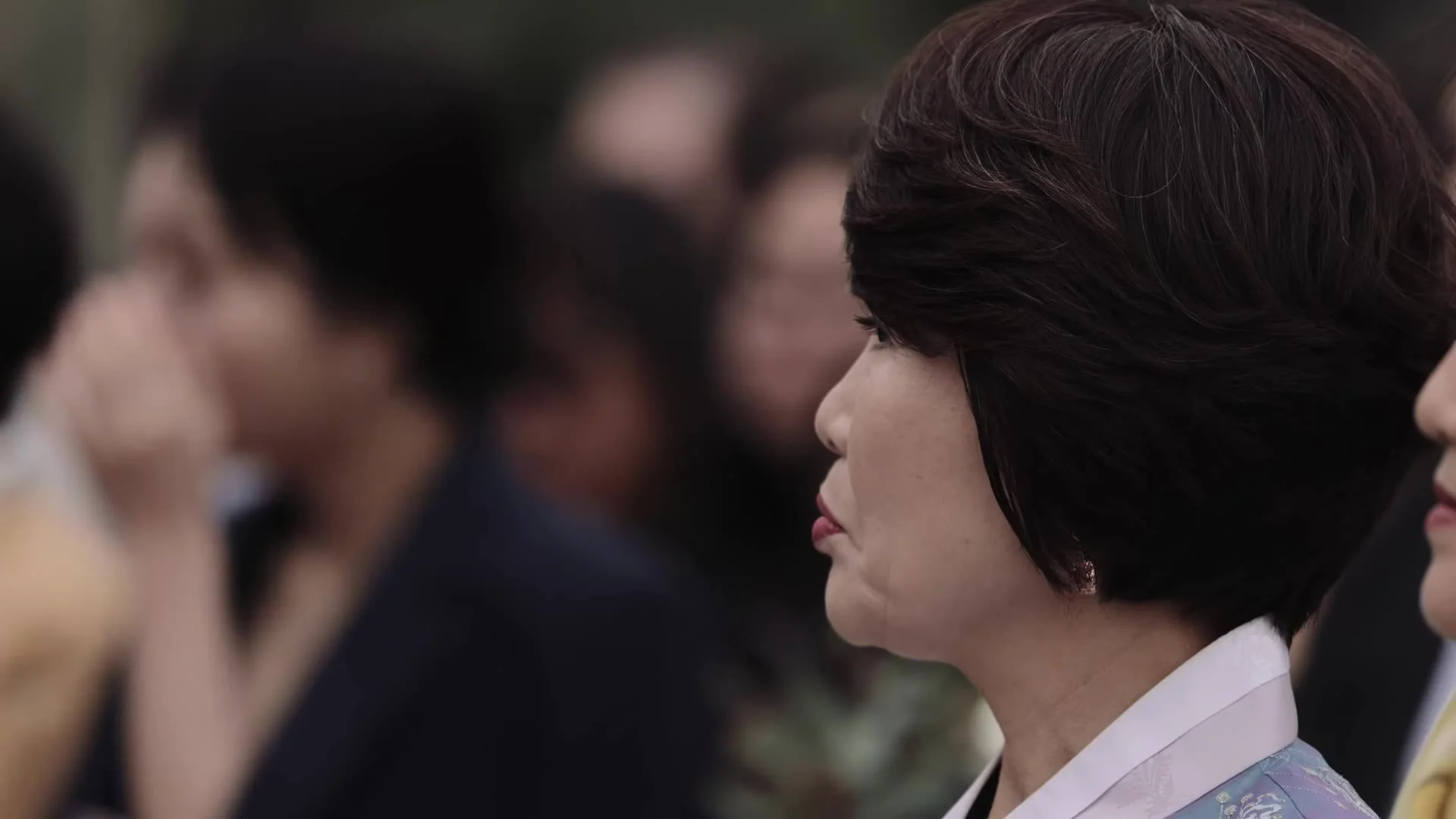 Profile of a guest in pale blue hanbok with white collar watching Manny and Jasmine's Korean wedding ceremony