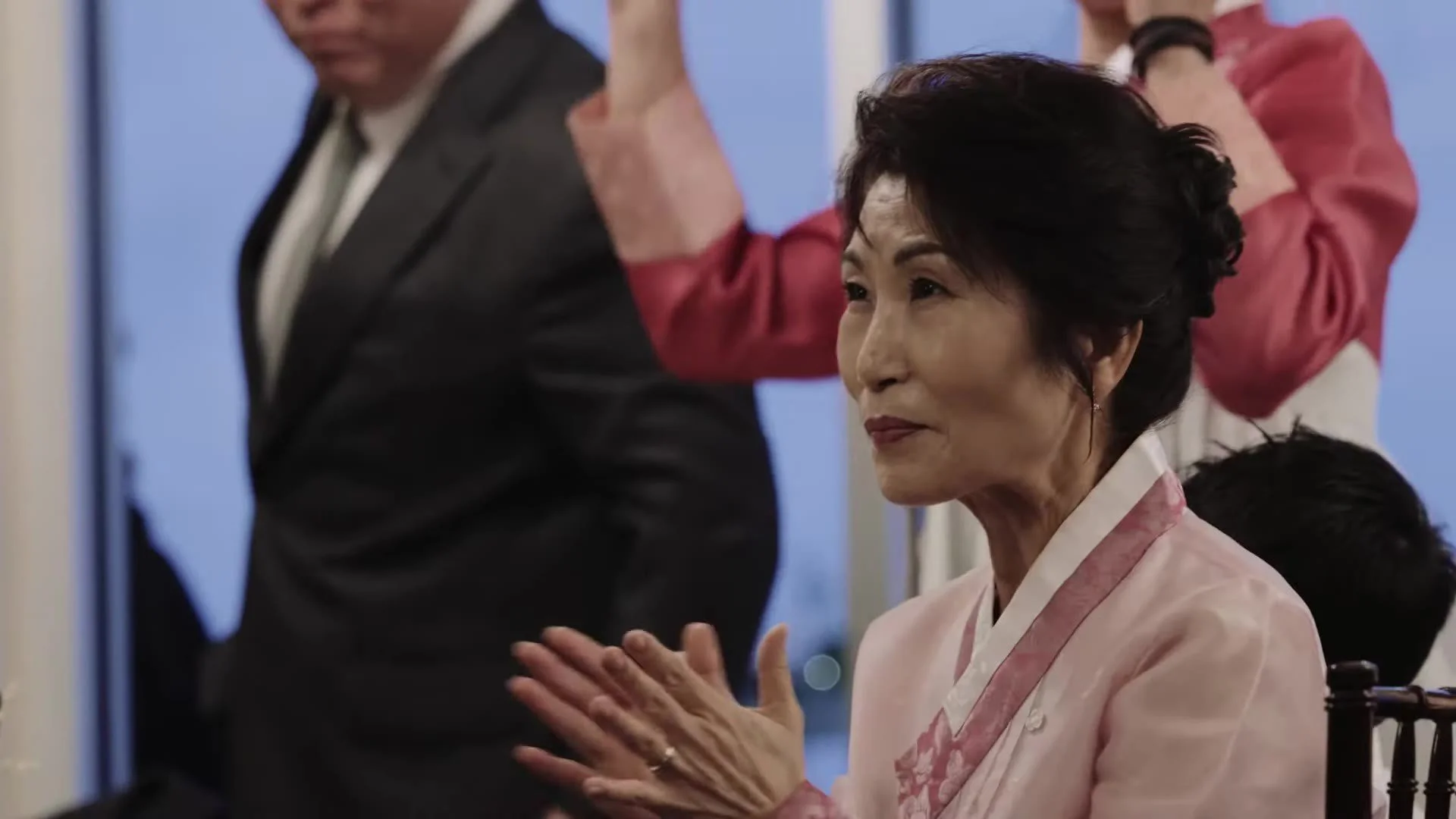 Guest in pale pink Korean hanbok smiling and clapping at Manny and Jasmine's Terrace Club reception