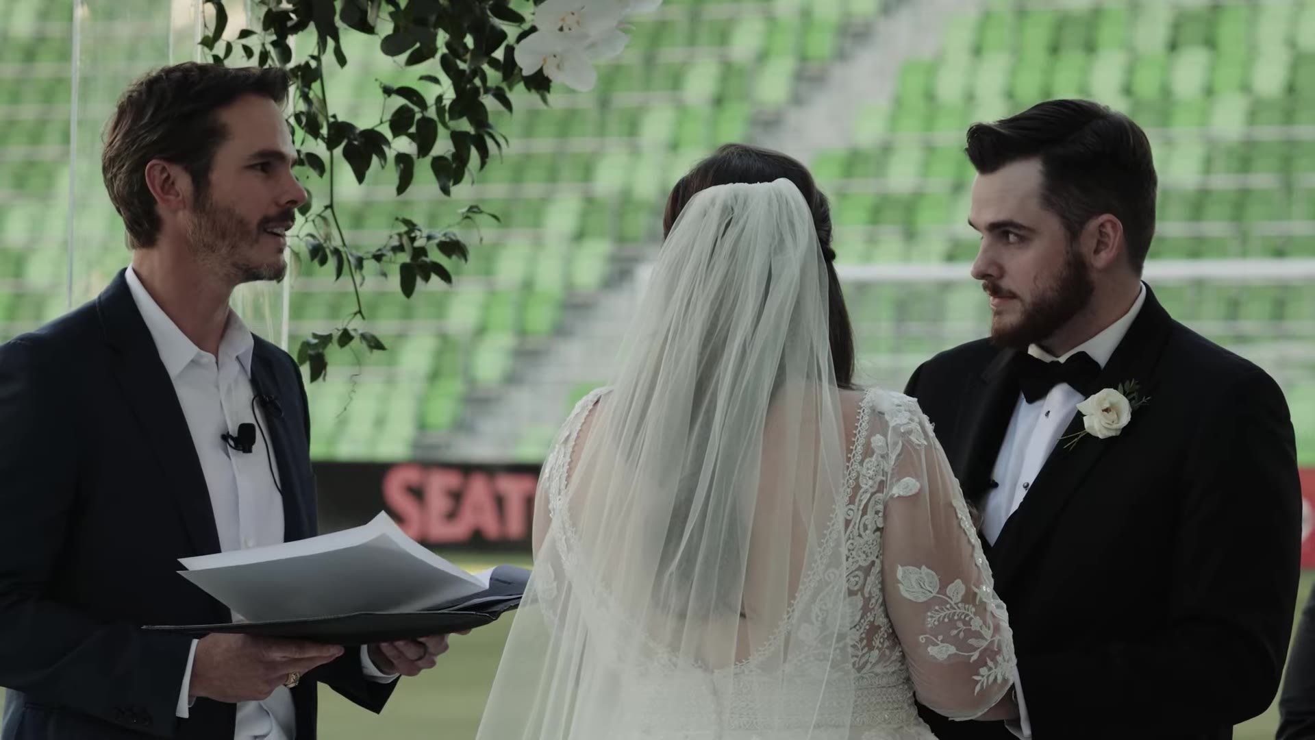 Gabby and Nic with their officiant during vows against green seats at Q2 Stadium in Austin, Texas