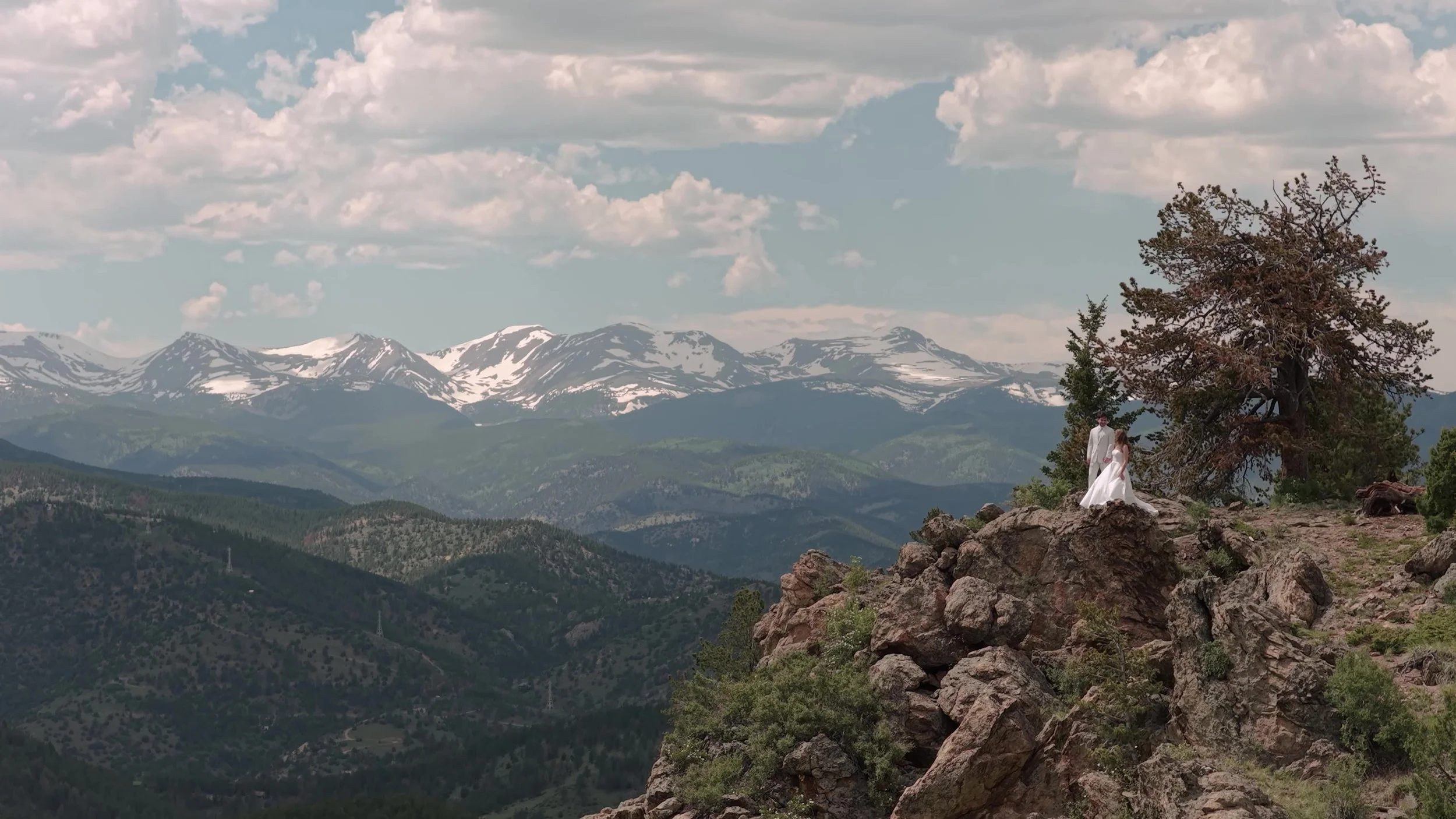 Bride in a white gown small on a rocky cliff overlooking snow-dusted peaks near Northstar Gatherings in Idaho Springs, Colorado