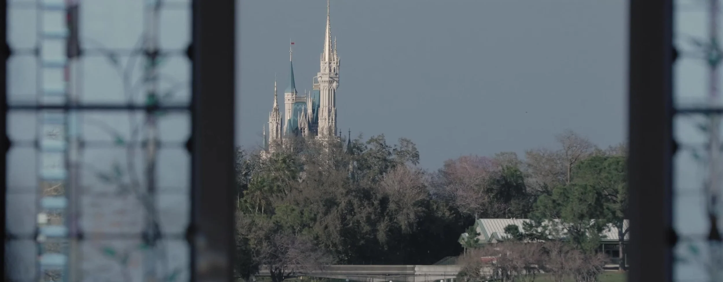 Cinderella Castle seen through a dark window frame, trees and a pale sky between the pavilion and Magic Kingdom