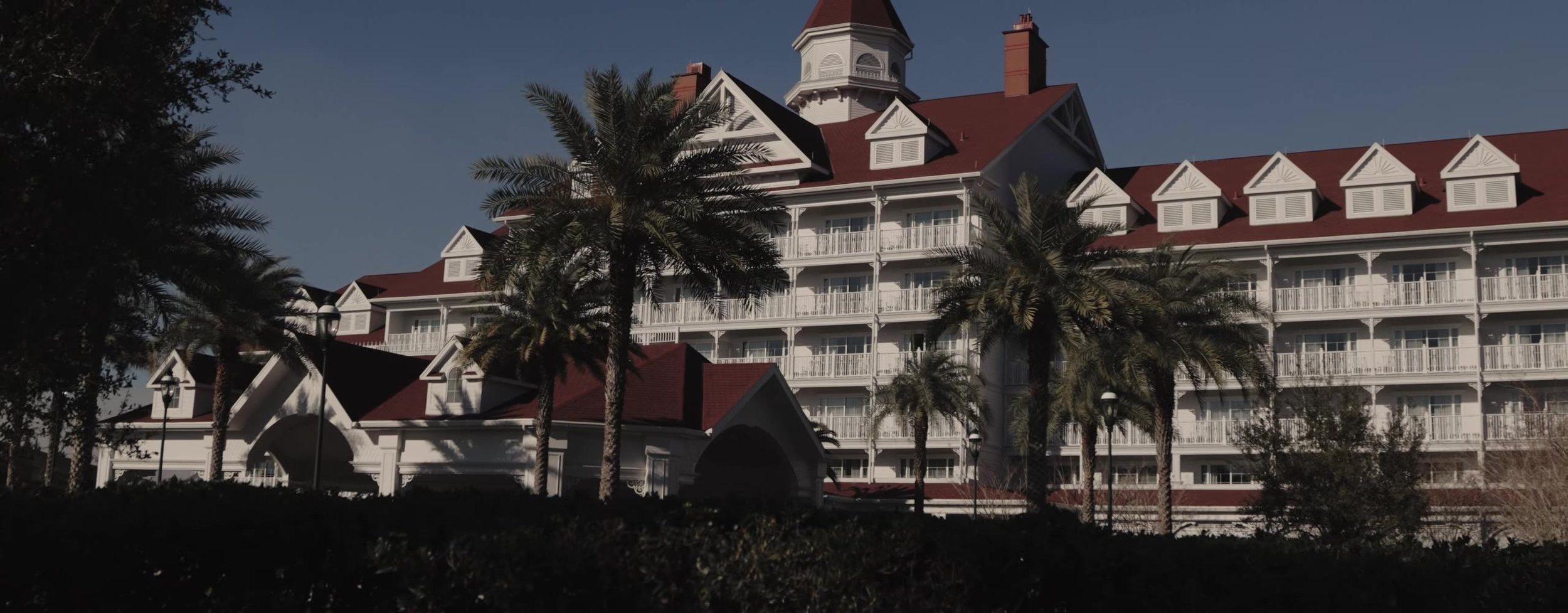 Exterior of Disney's Grand Floridian Resort, white Victorian wings and red roofs behind palm trees