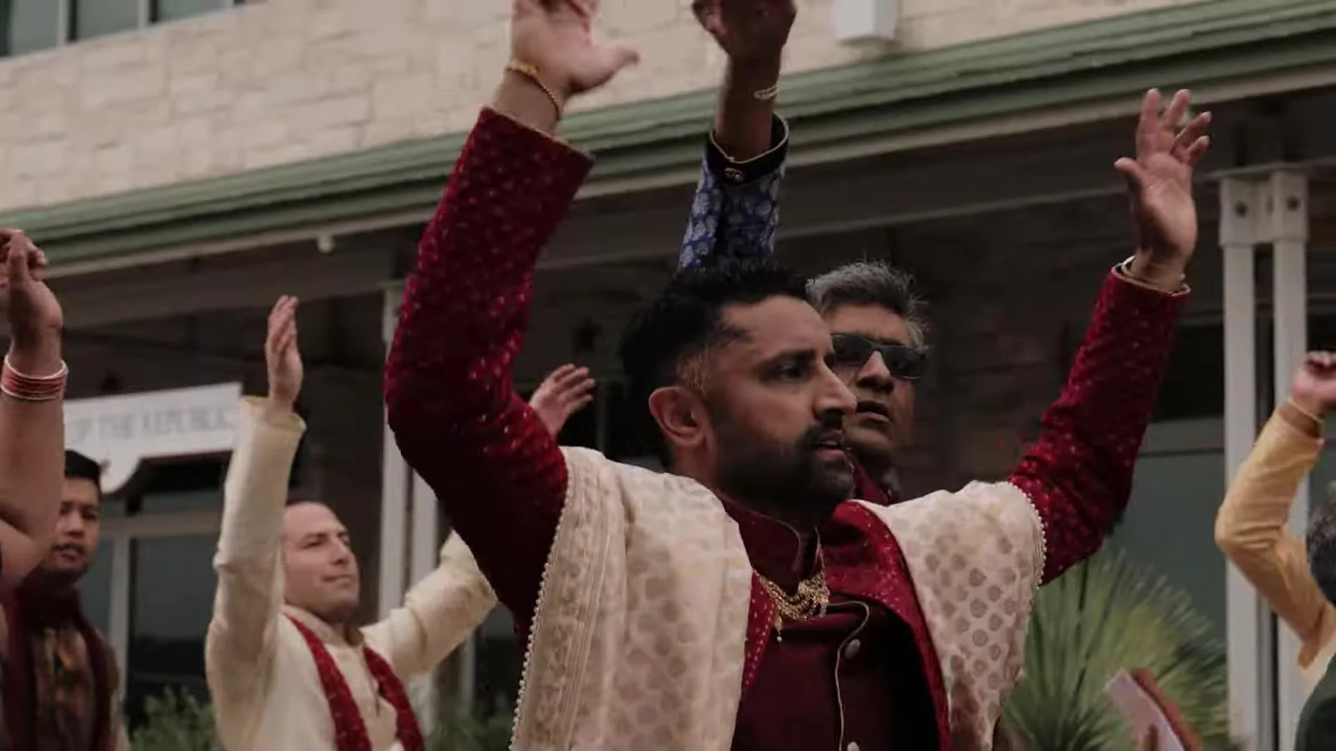 Bhavim in a red sherwani and cream gold dupatta dancing with arms raised during the baraat at The Terrace Club in Austin