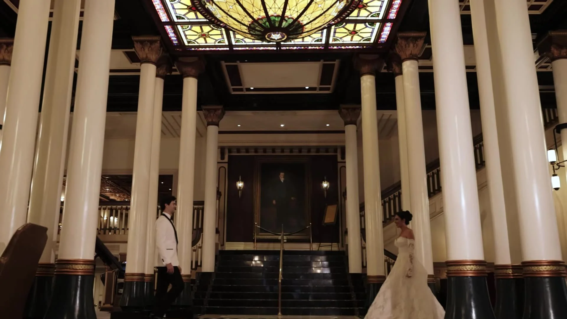 High angle of Grant and Anna between columns and the staircase under The Driskill stained glass dome in Austin