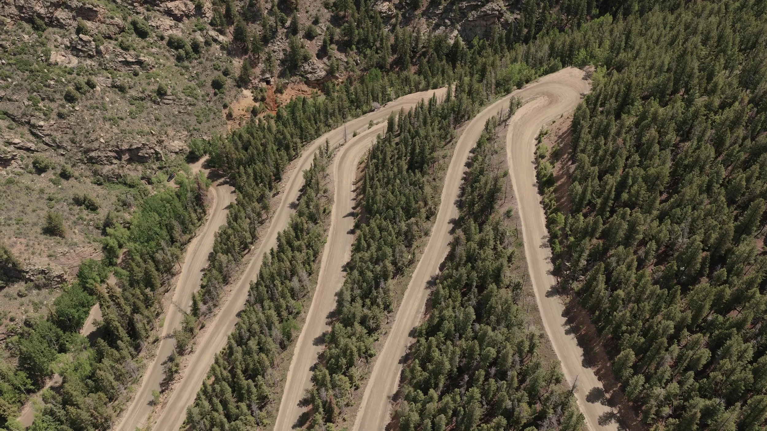 Aerial view of dirt switchbacks through pine forest on the mountain road to Northstar Gatherings near Idaho Springs, Colorado
