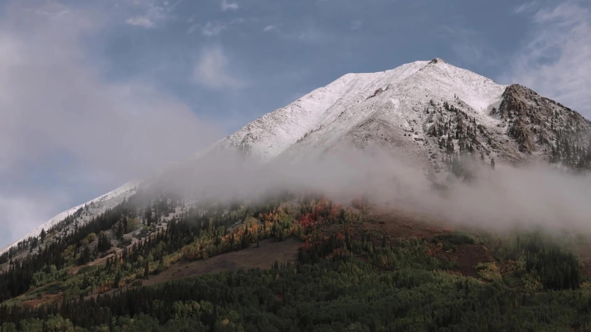 Snowcapped Crested Butte peak with autumn aspen and cloud wrapped slopes in Colorado