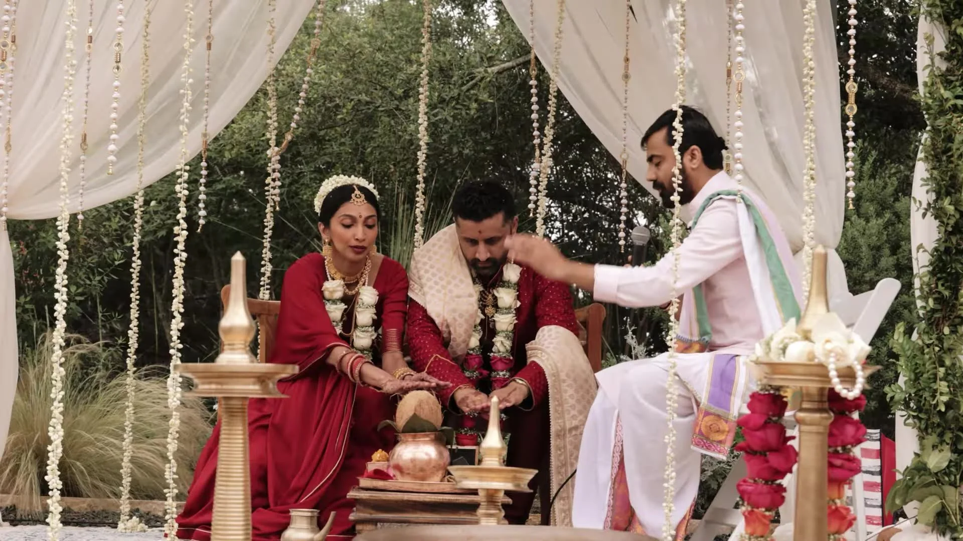 Bhavim and Mala seated with a priest under hanging flower strands with kalash and brass lamps at The Terrace Club in Austin
