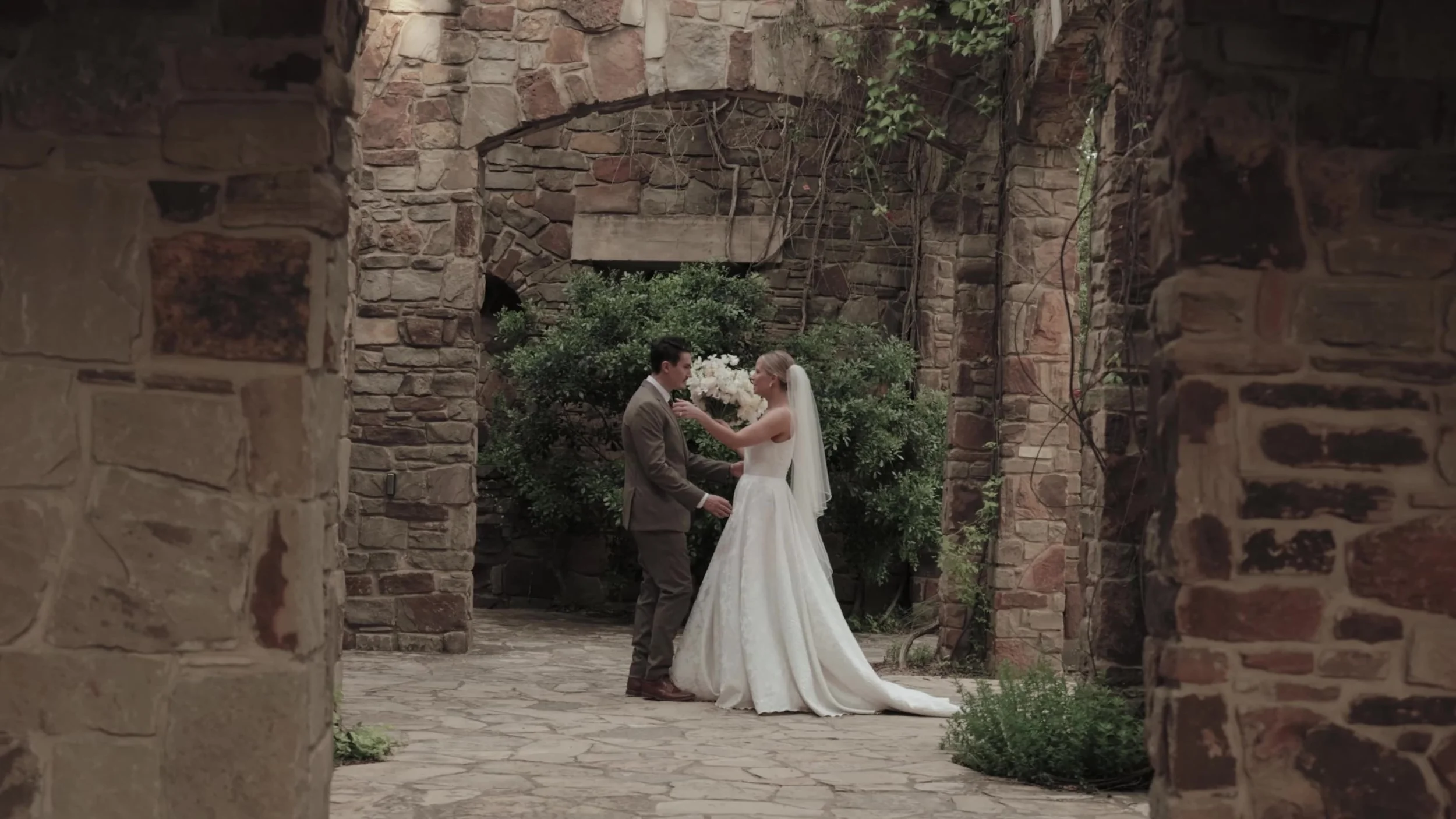 Heather and Chris in a stone courtyard as she adjusts his boutonniere at Lady Bird Johnson Wildflower Center in Austin, Texas