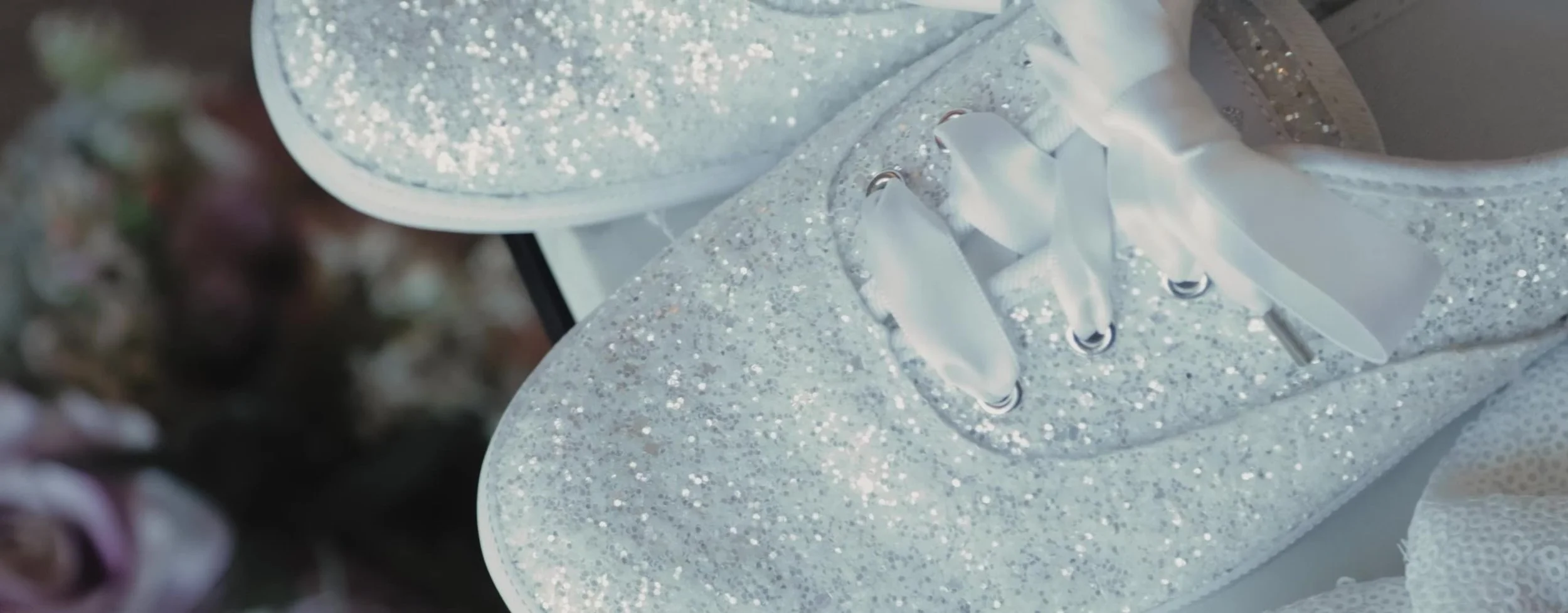 White glitter bridal sneakers with satin ribbon laces, bouquet soft in the background