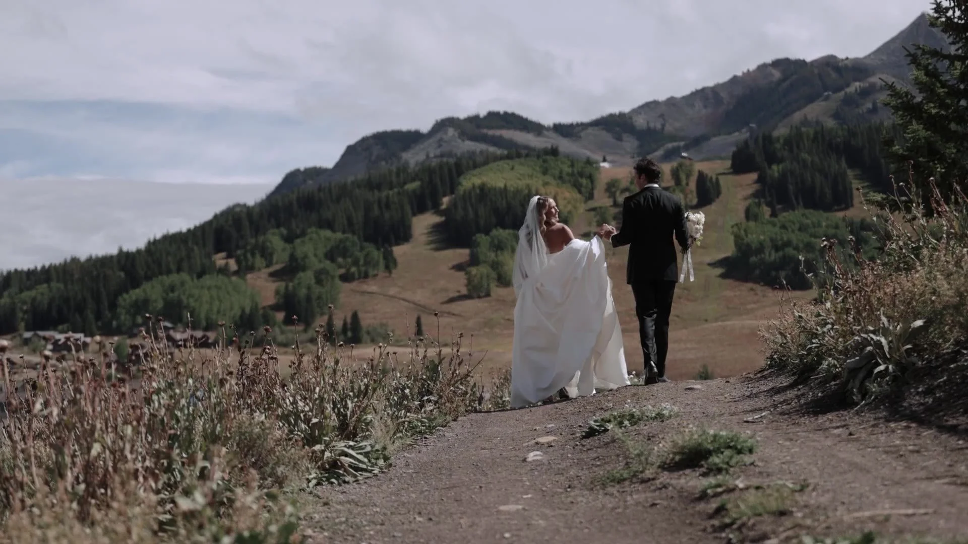 Becca and Colton walking a dirt road toward the mountains near Crested Butte Wedding Garden in Colorado