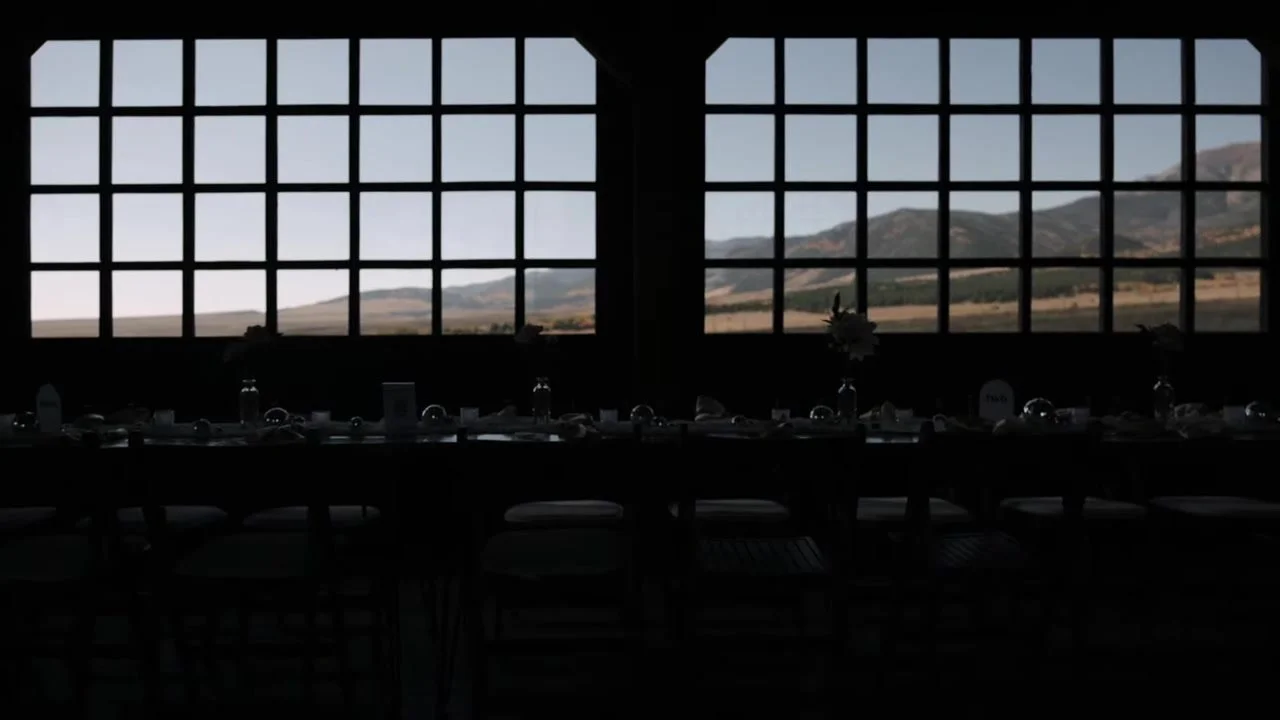 Silhouetted reception table and chairs in front of large grid windows overlooking the Wet Mountains