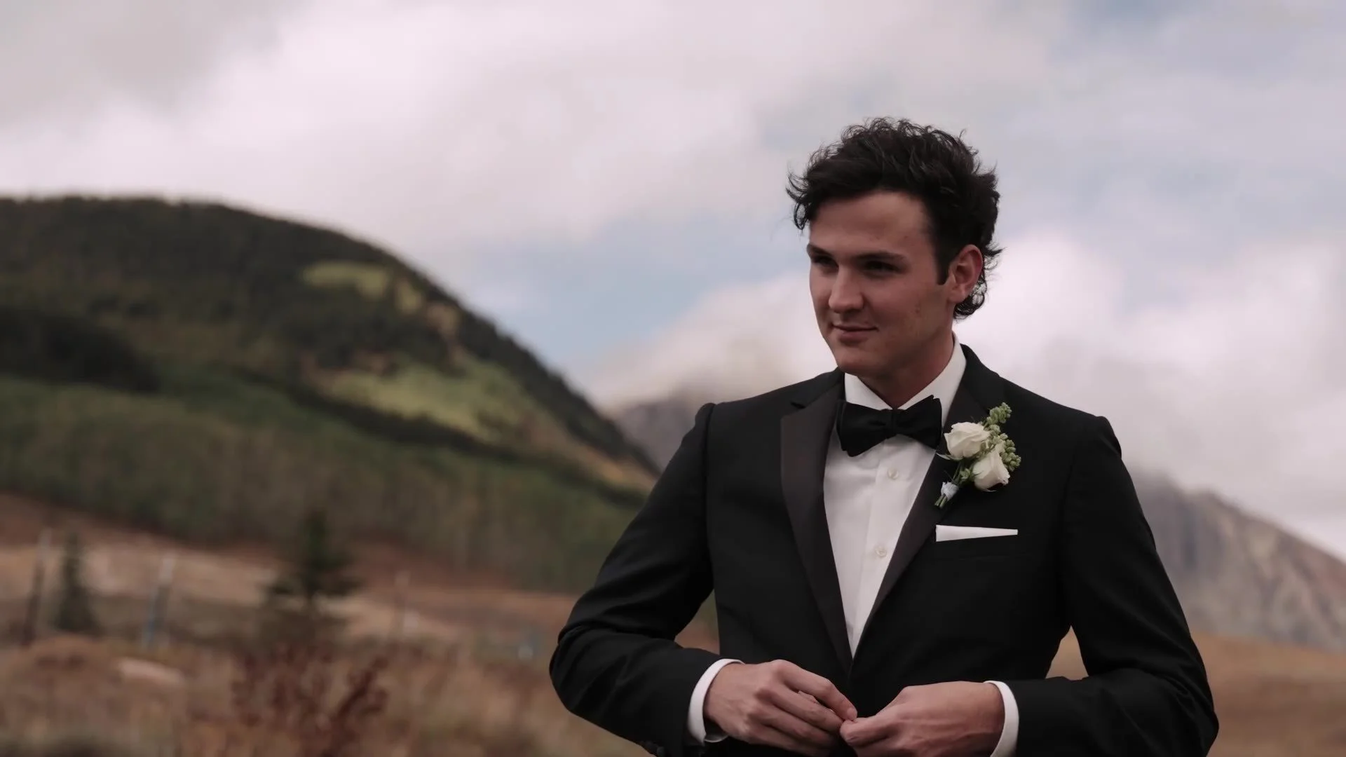 Groom in a black tuxedo and bow tie against Colorado mountains at Crested Butte Wedding Garden