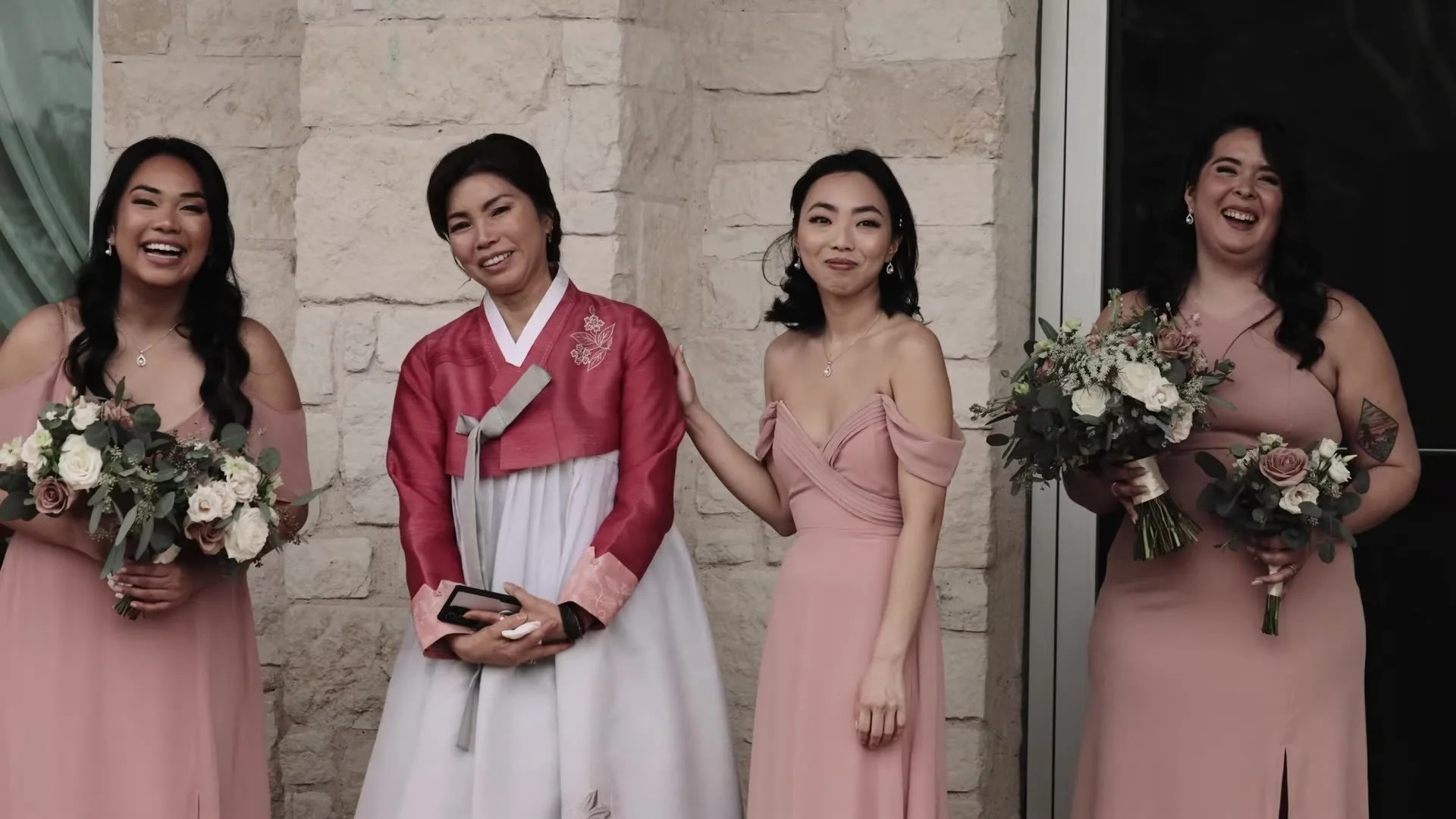 Woman in magenta and white hanbok with bridesmaids in dusty rose against a stone wall at The Terrace Club
