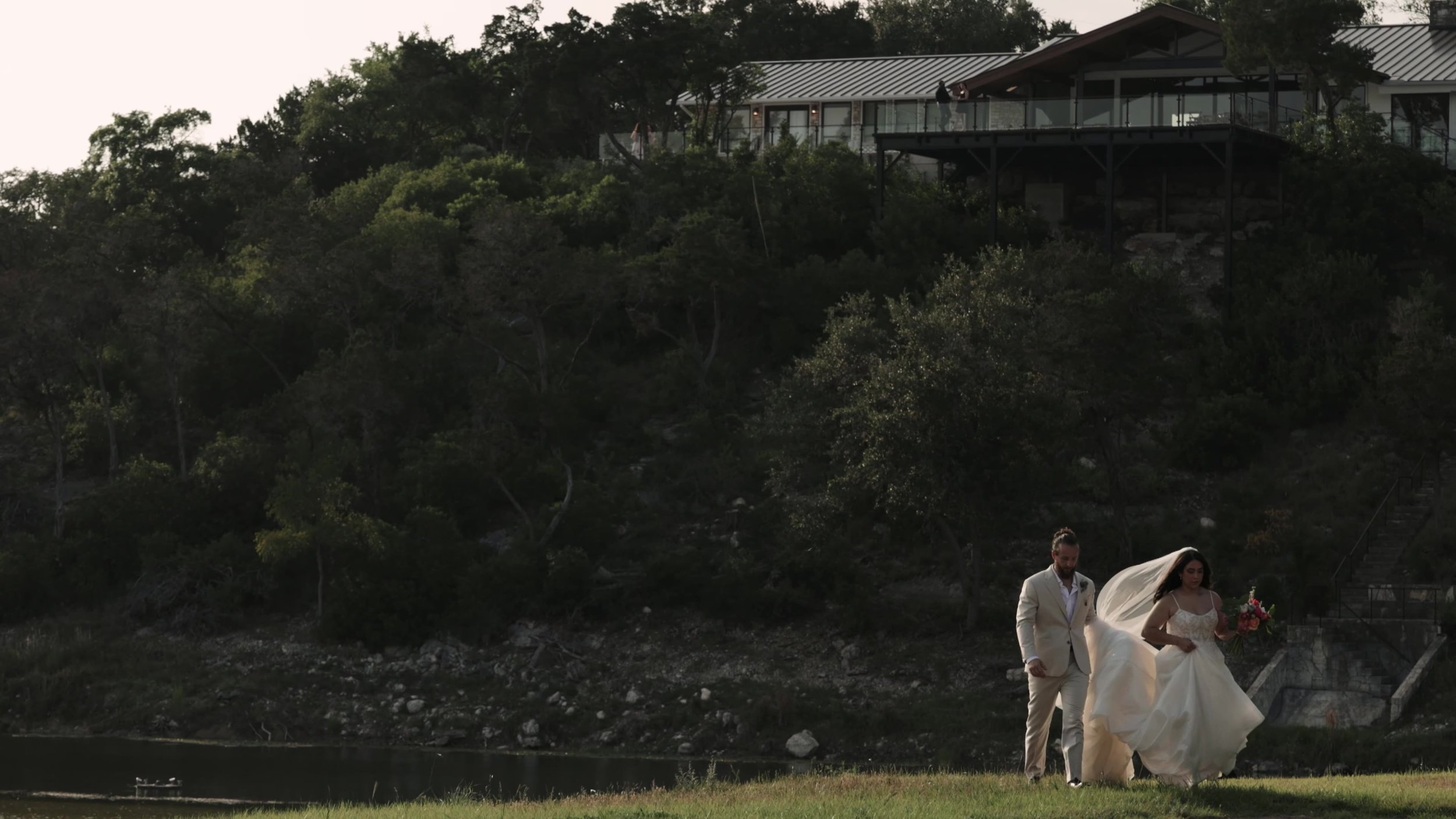 Peter and Kiyara walking a wide lawn below the modern estate on the hill at Videre Estate in Texas Hill Country near Austin