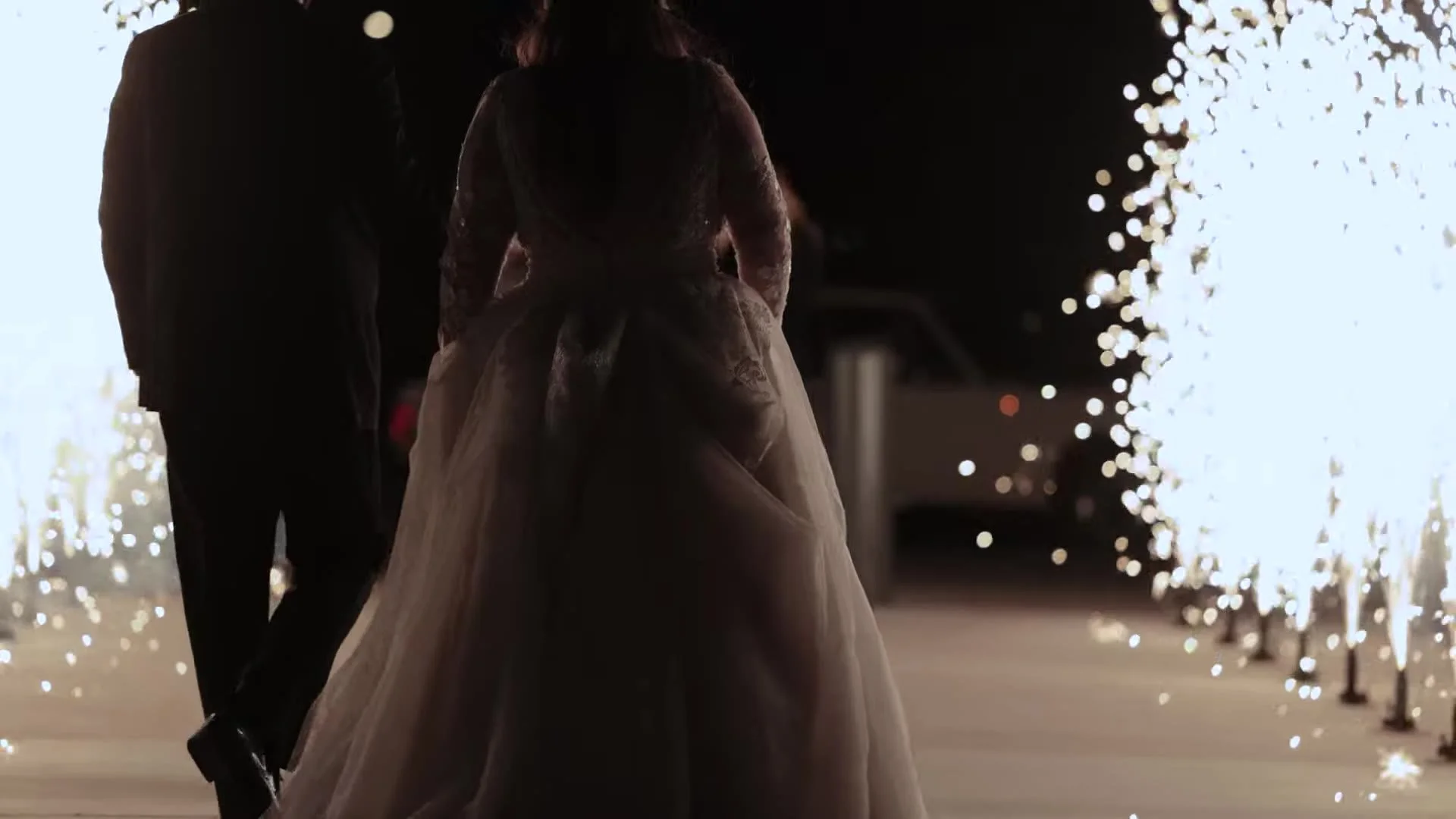 Gabby and Nic walking through cold sparkler fountains at night after their Q2 Stadium wedding in Austin