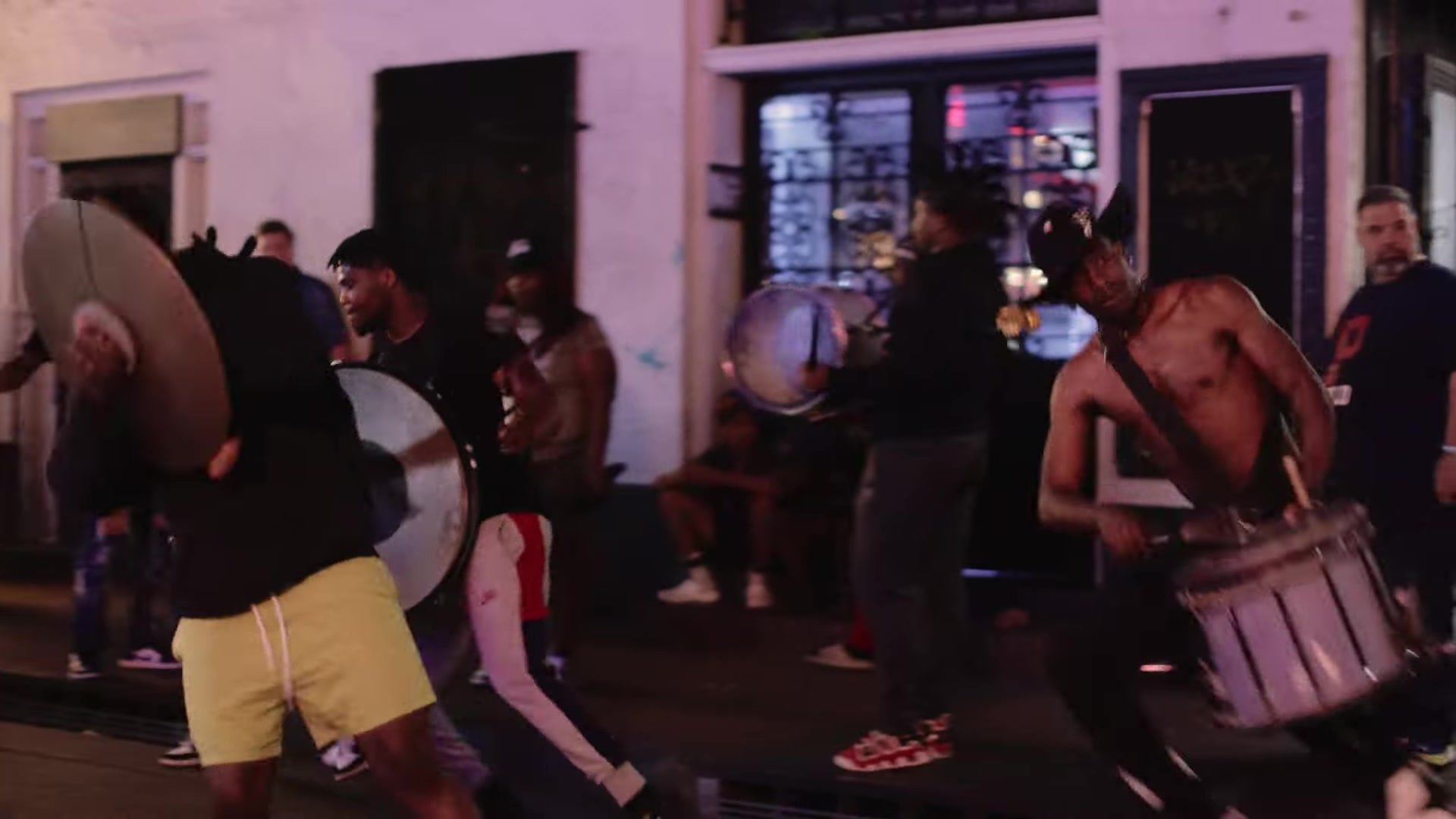 Street percussionists with drums and metal lids on a French Quarter sidewalk at night in New Orleans