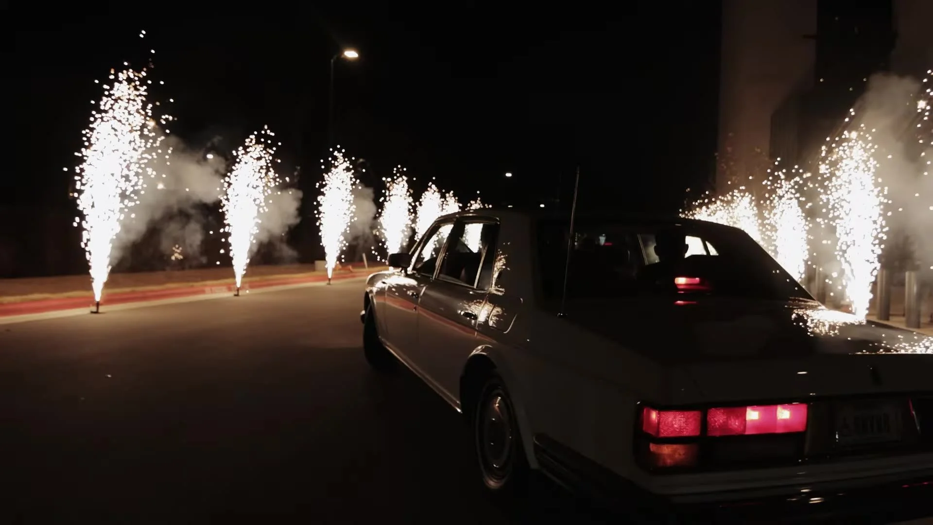 White vintage getaway car driving between sparkler fountains at night outside Q2 Stadium in Austin, Texas