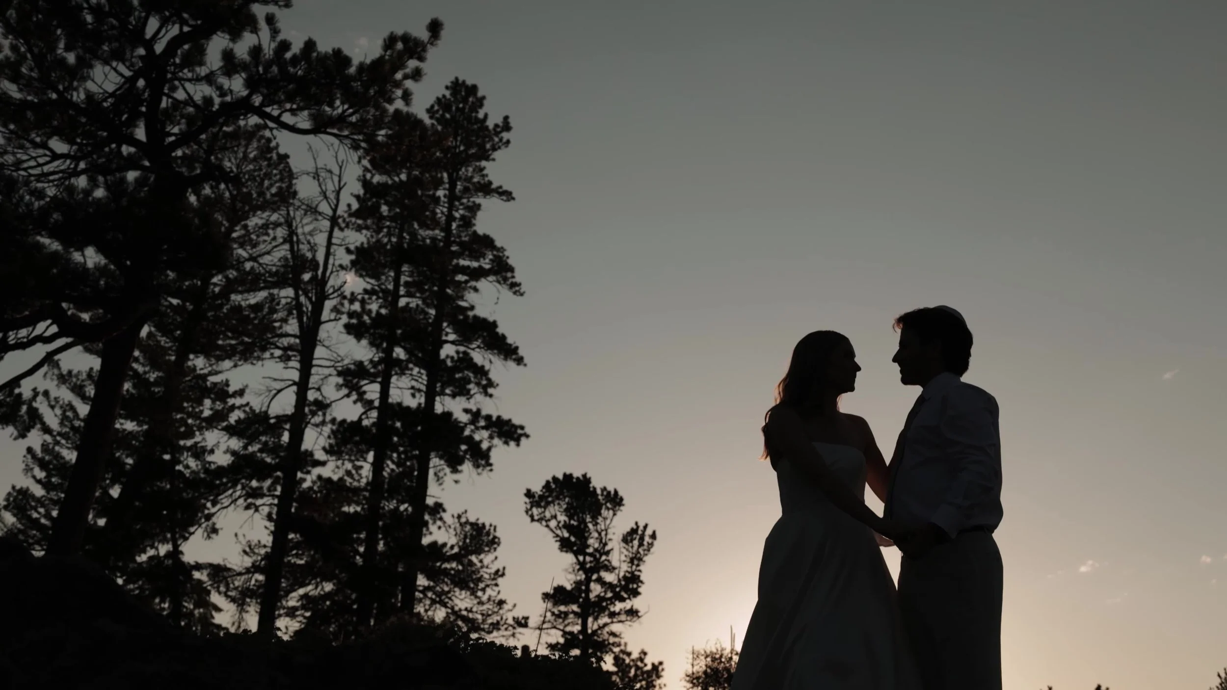 Silhouette of the couple among pines at dusk at Northstar Gatherings in Idaho Springs, Colorado