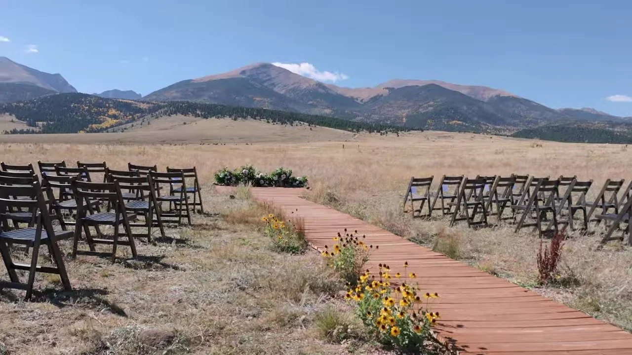 Empty wooden plank aisle through golden grass toward mountain peaks at 3 Peaks Ranch