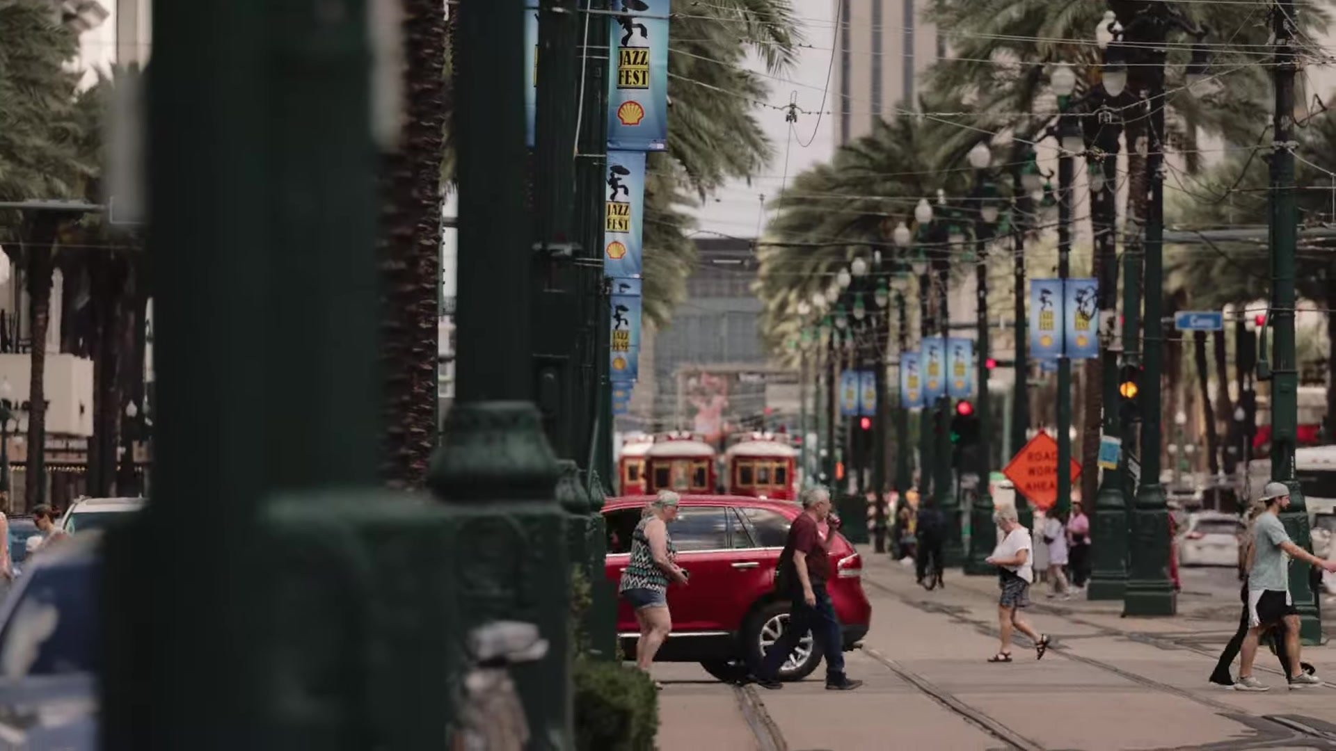 Jazz Fest banners and red streetcars on a palm lined New Orleans street during Jazz Fest weekend